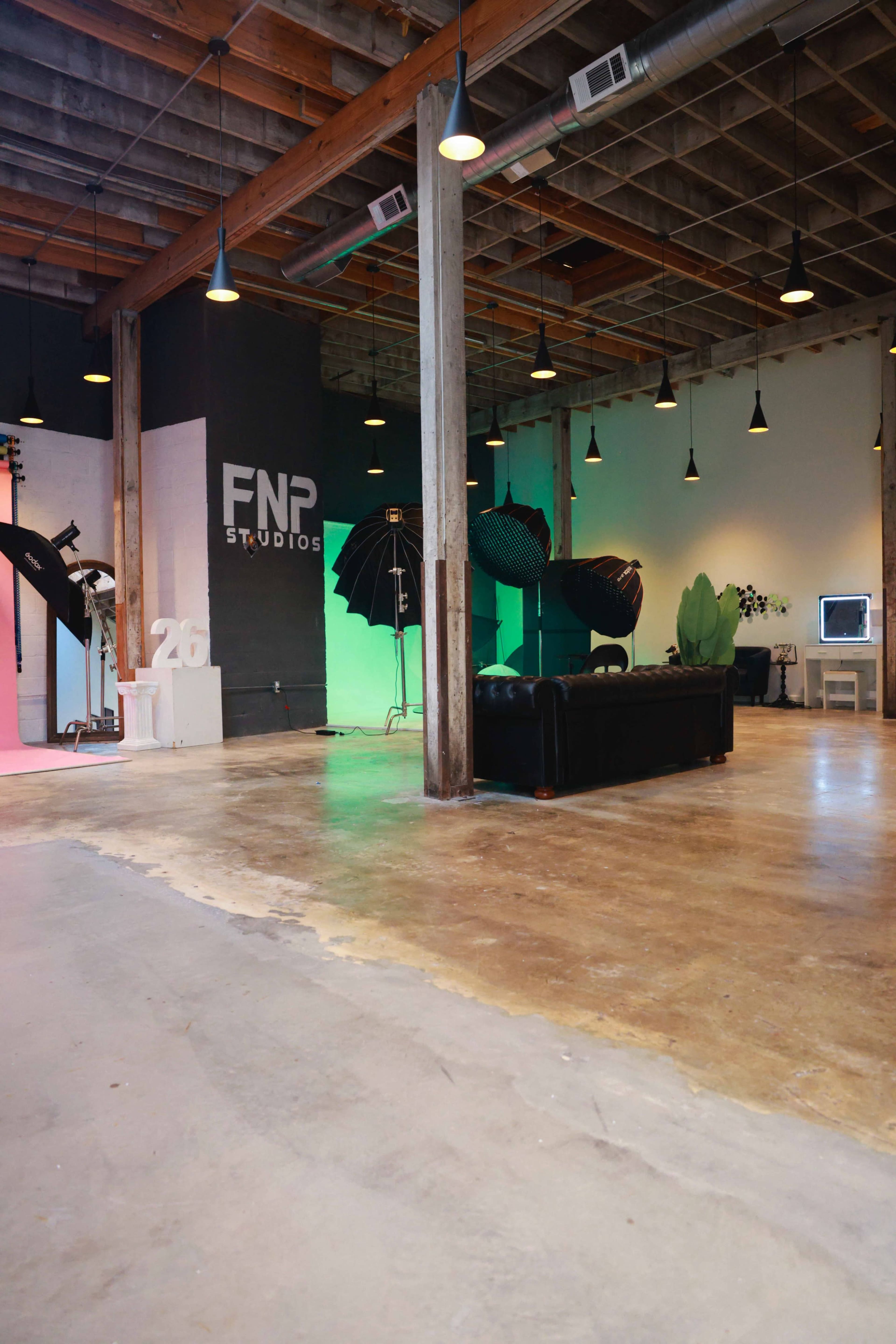 The image shows a spacious studio with wooden beams, a polished concrete floor, and various photography equipment, including lights and backdrops.