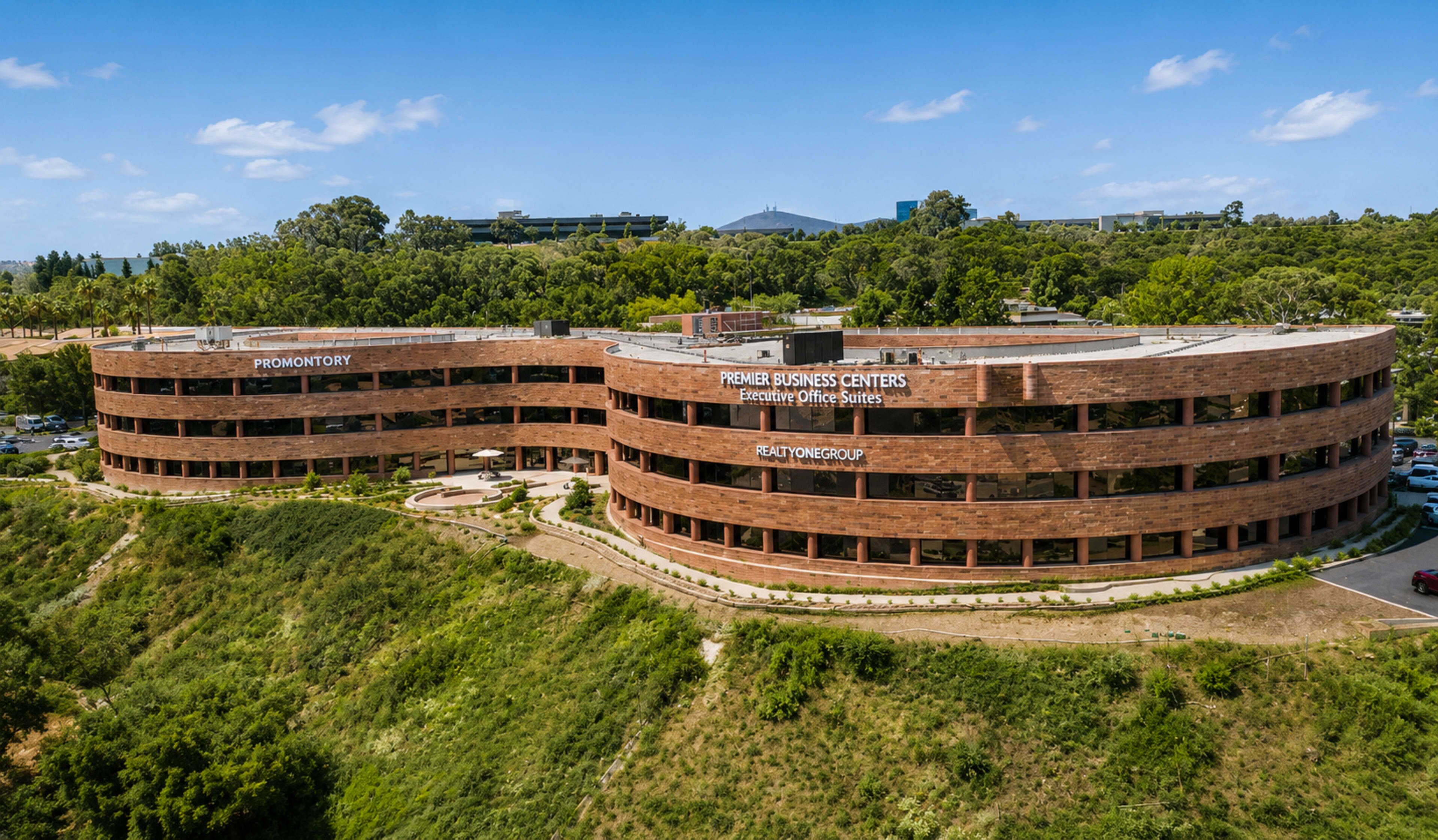 The image shows a multi-story office building with a rounded design, surrounded by greenery and a parking lot.