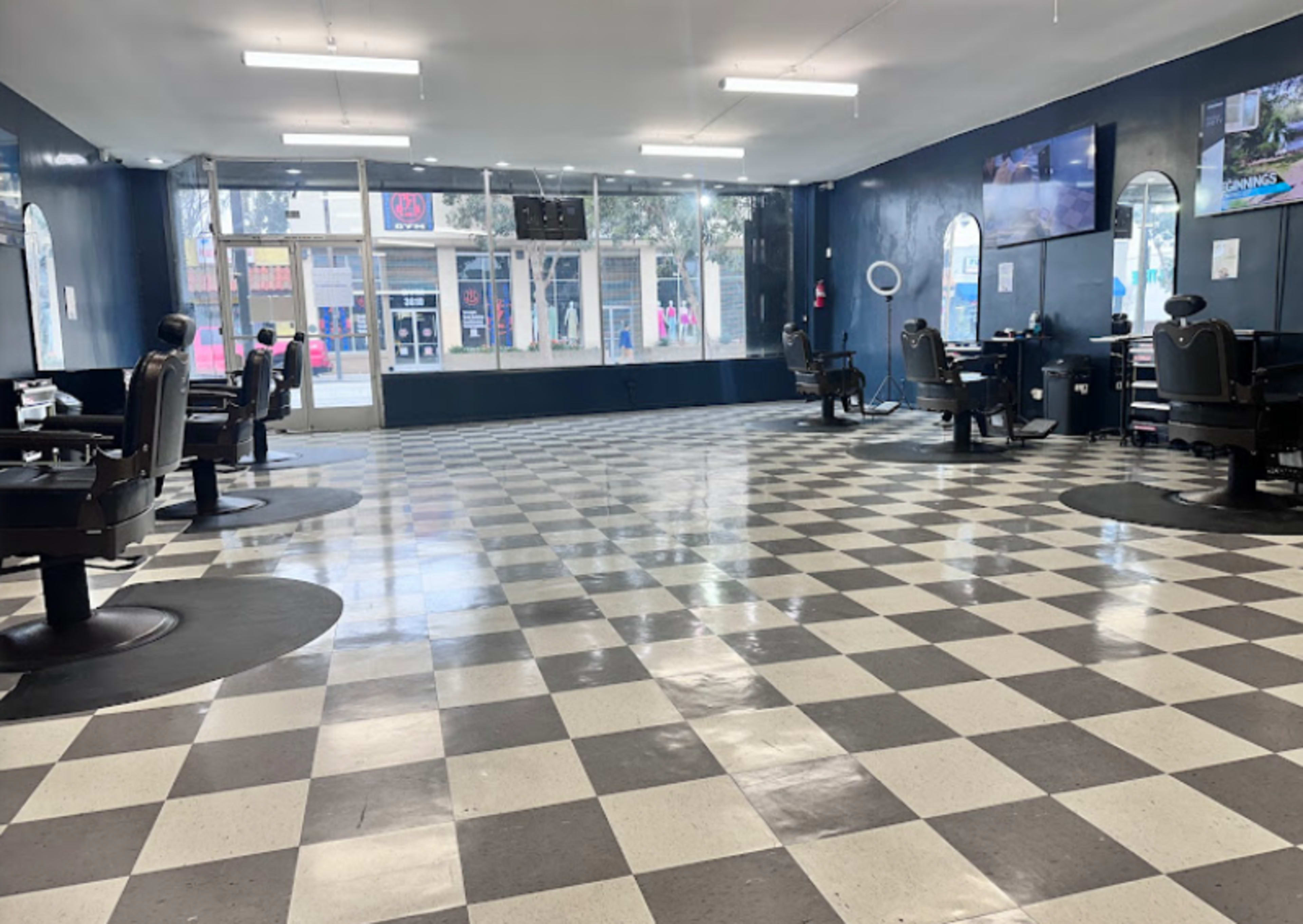 The image shows the interior of a barbershop with black and white checkered flooring, several barber chairs, and large windows facing the street.