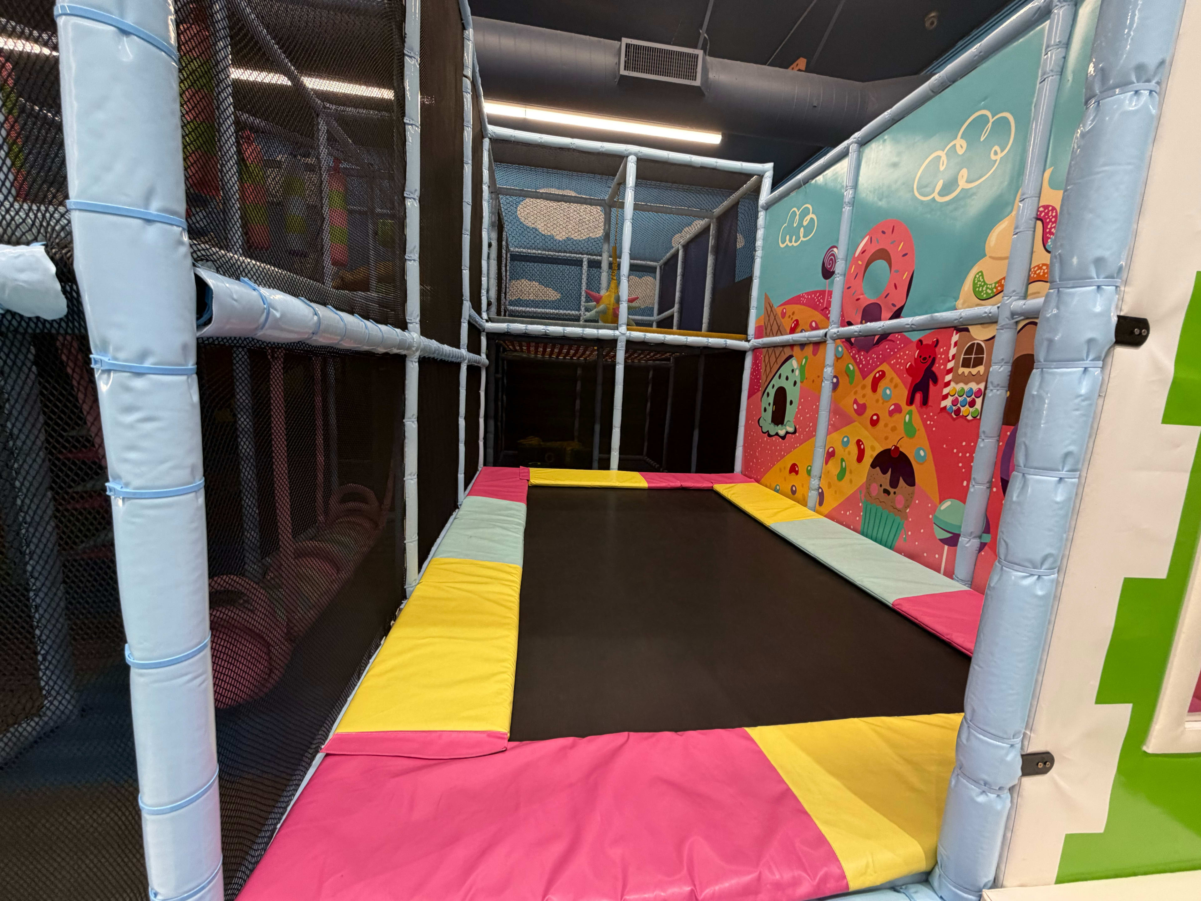 The image shows an indoor trampoline area with colorful padding and mesh safety barriers.