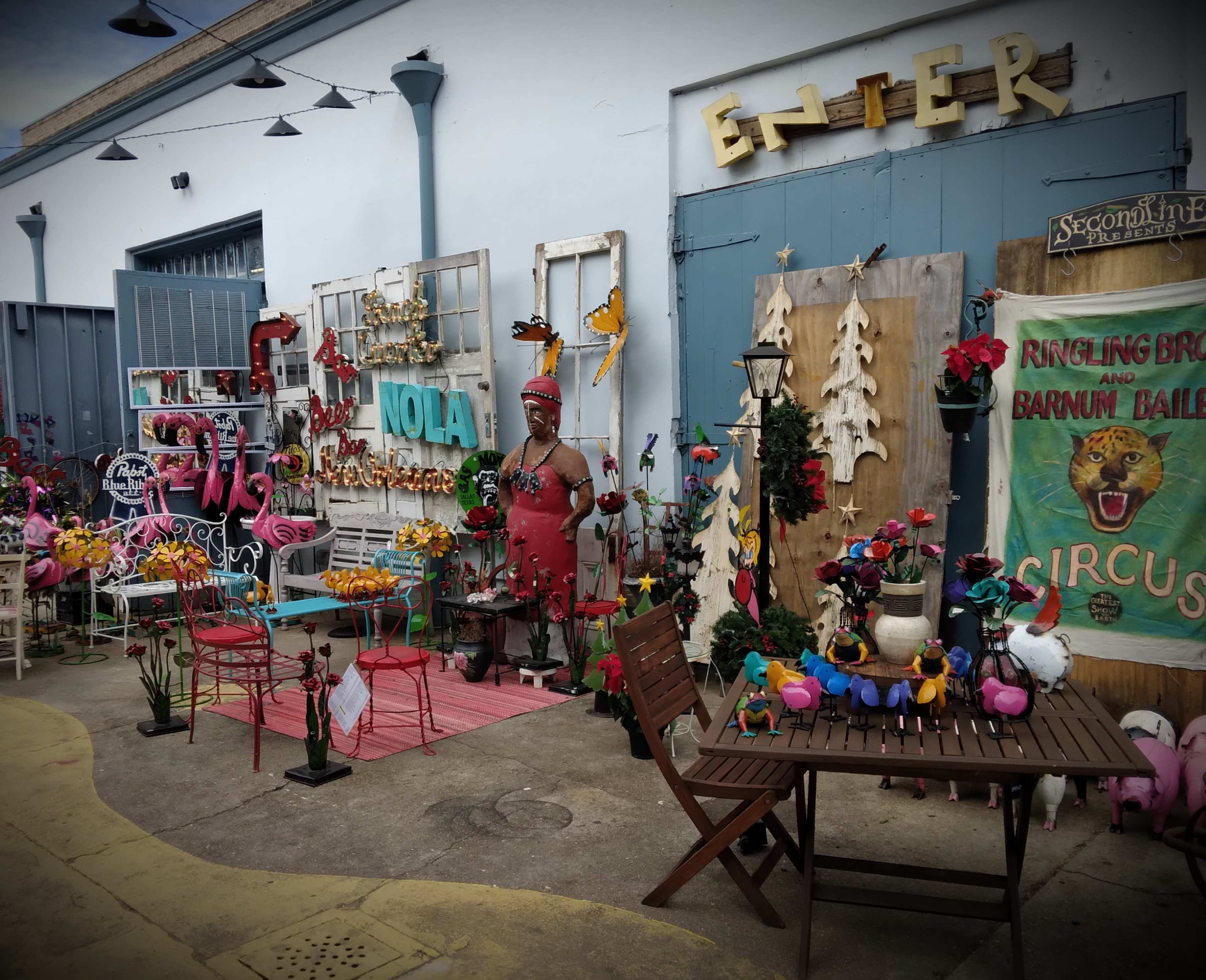 The scene features a vibrant outdoor decor shop with colorful ornaments, including flamingos and circus-themed displays, along with various seating arrangements.