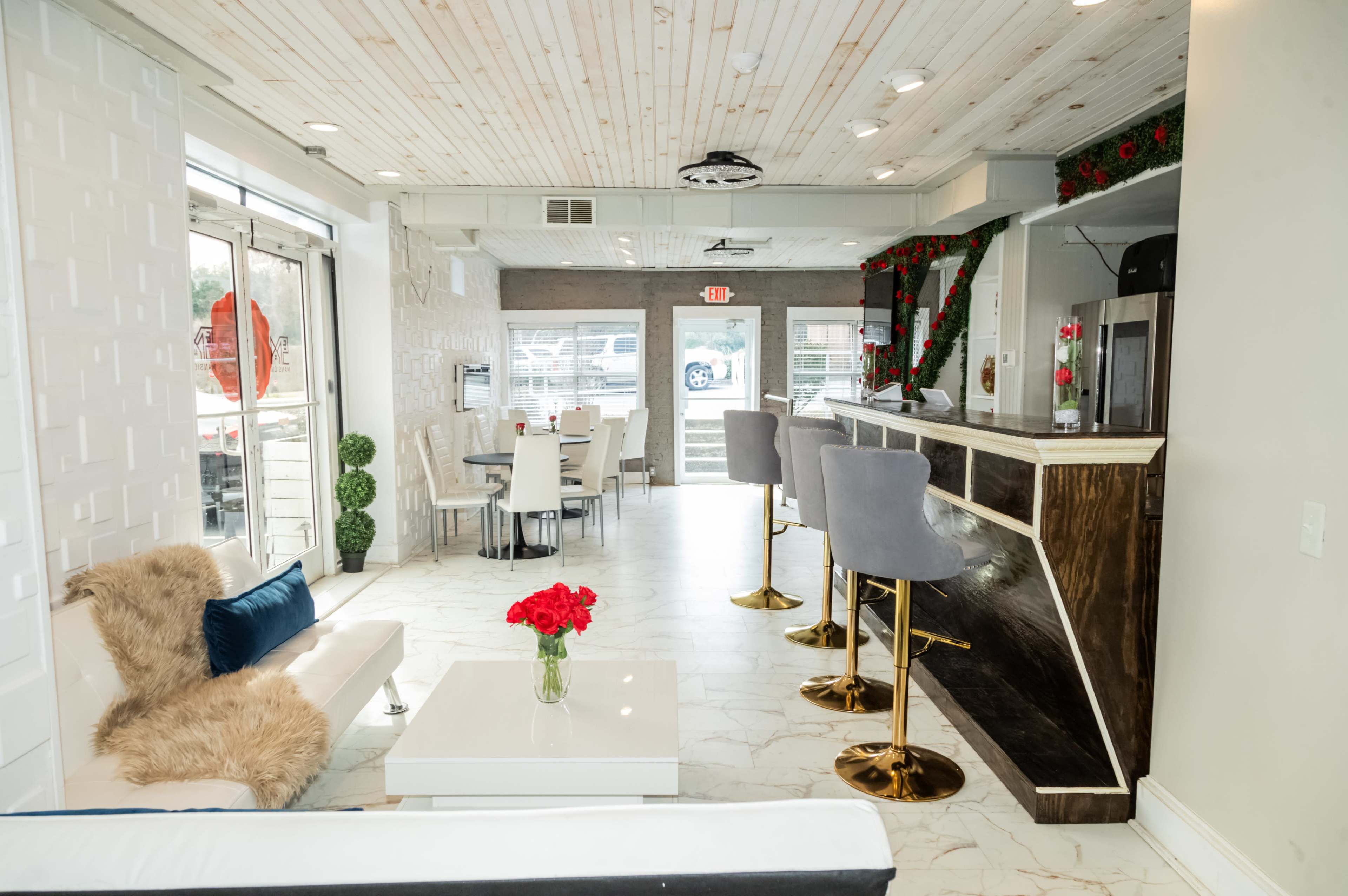 The image shows a modern café interior featuring white and wood paneling, a cozy seating area with a sofa, and a bar counter with tall stools.