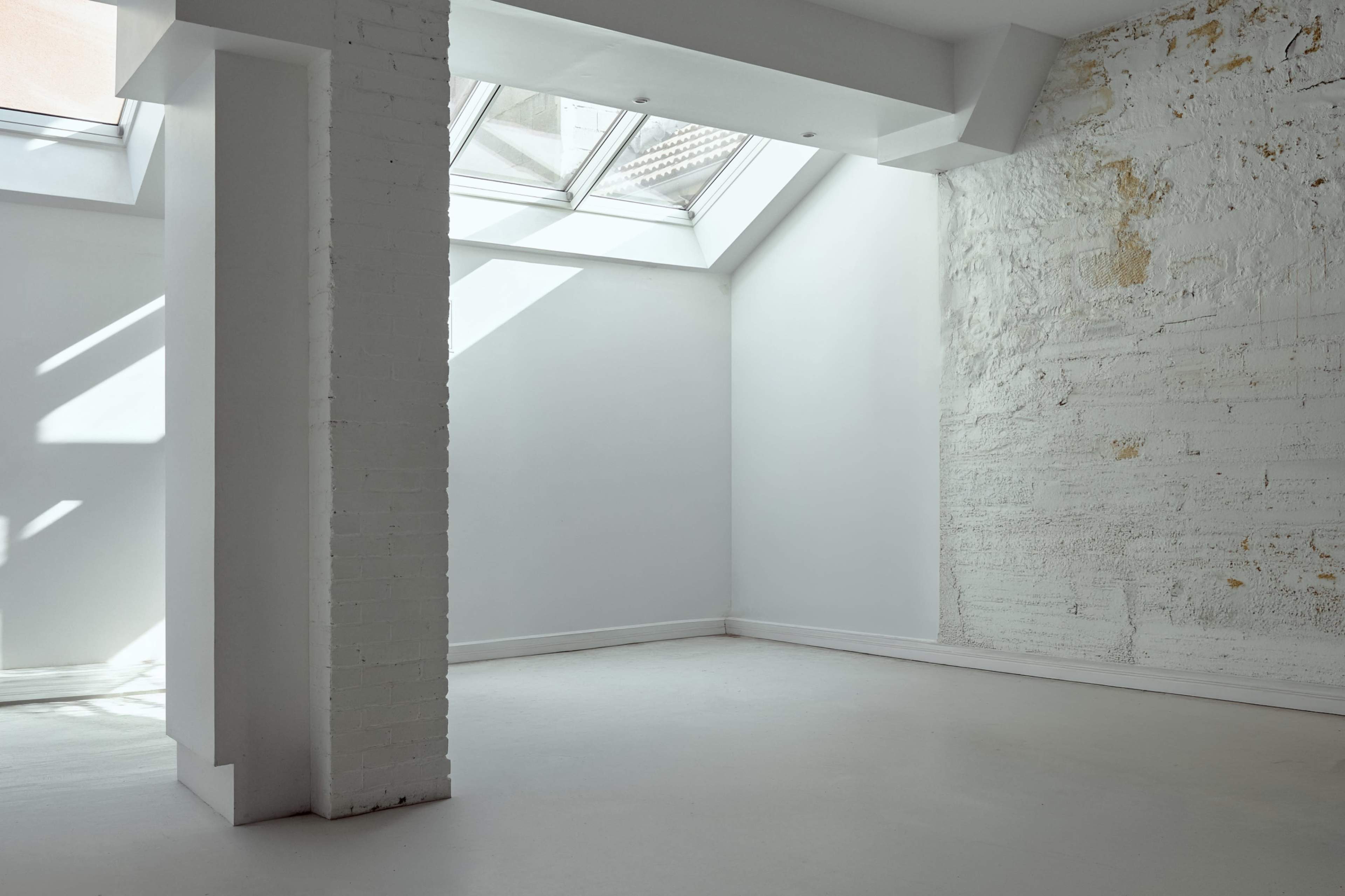 The image depicts an empty room with white walls, a skylight, and a textured wall in one corner.