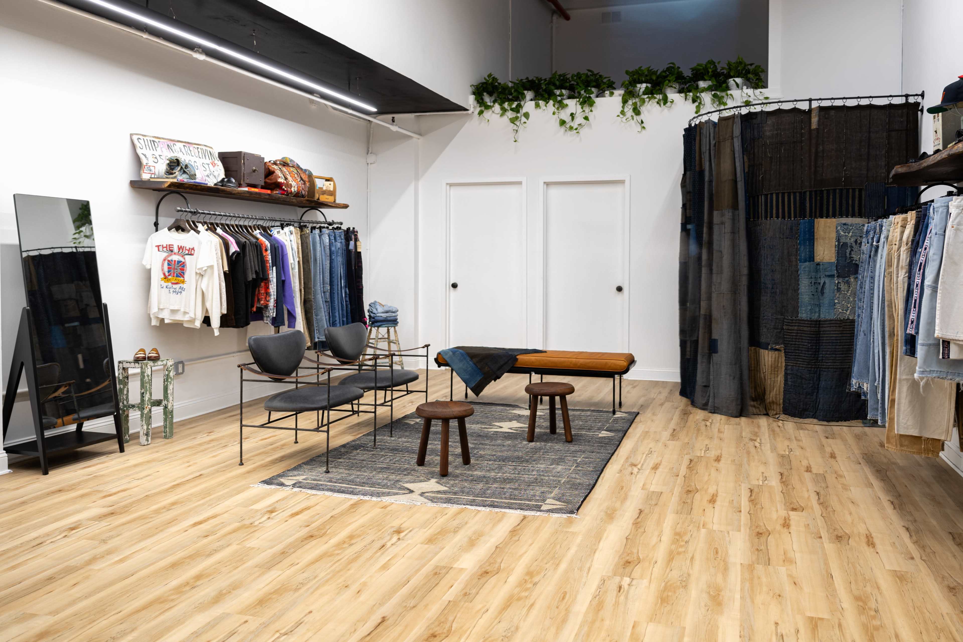 The image shows a modern clothing store interior with racks of denim and apparel, a mirror, a wooden bench, and a patterned rug.