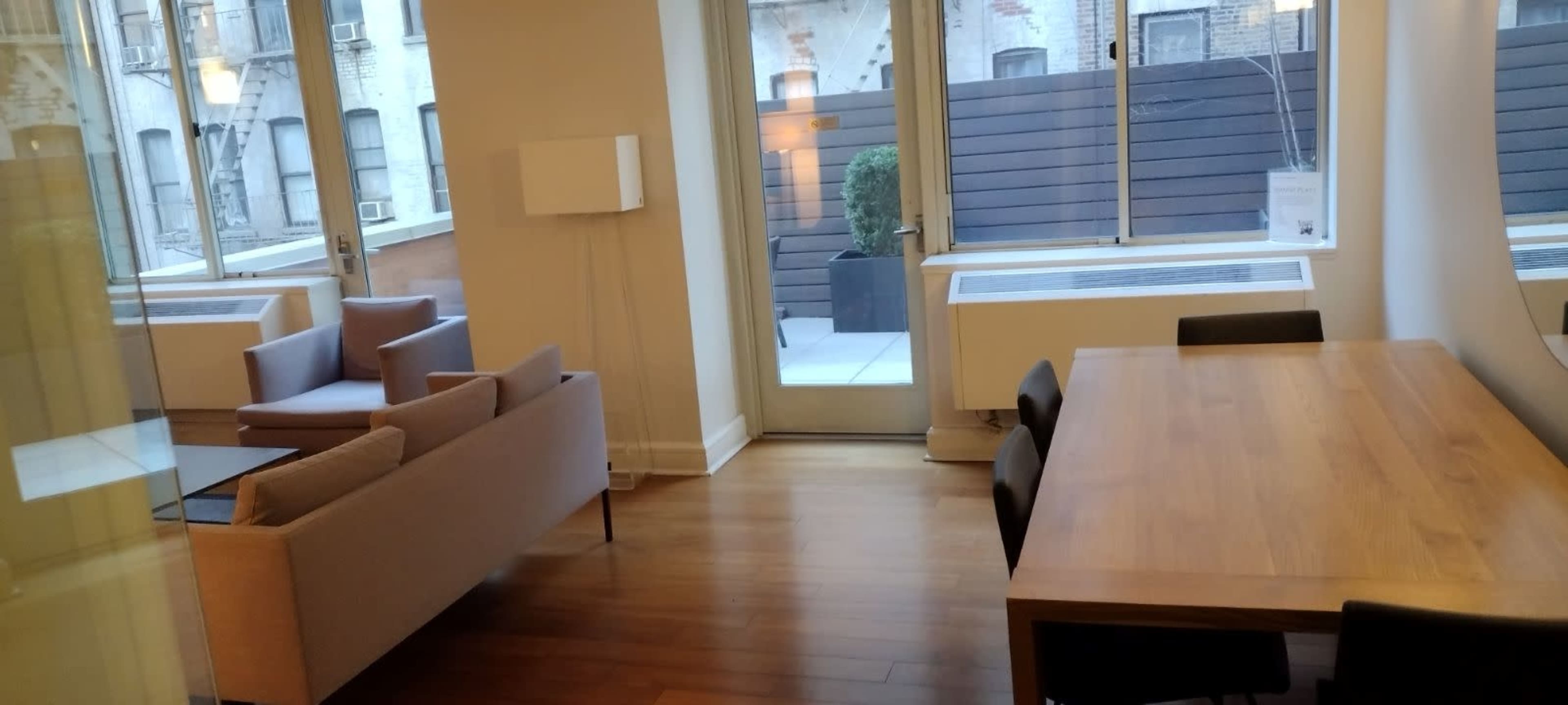 A modern living space with a sofa, a dining table, and large windows looking out onto a small outdoor area.
