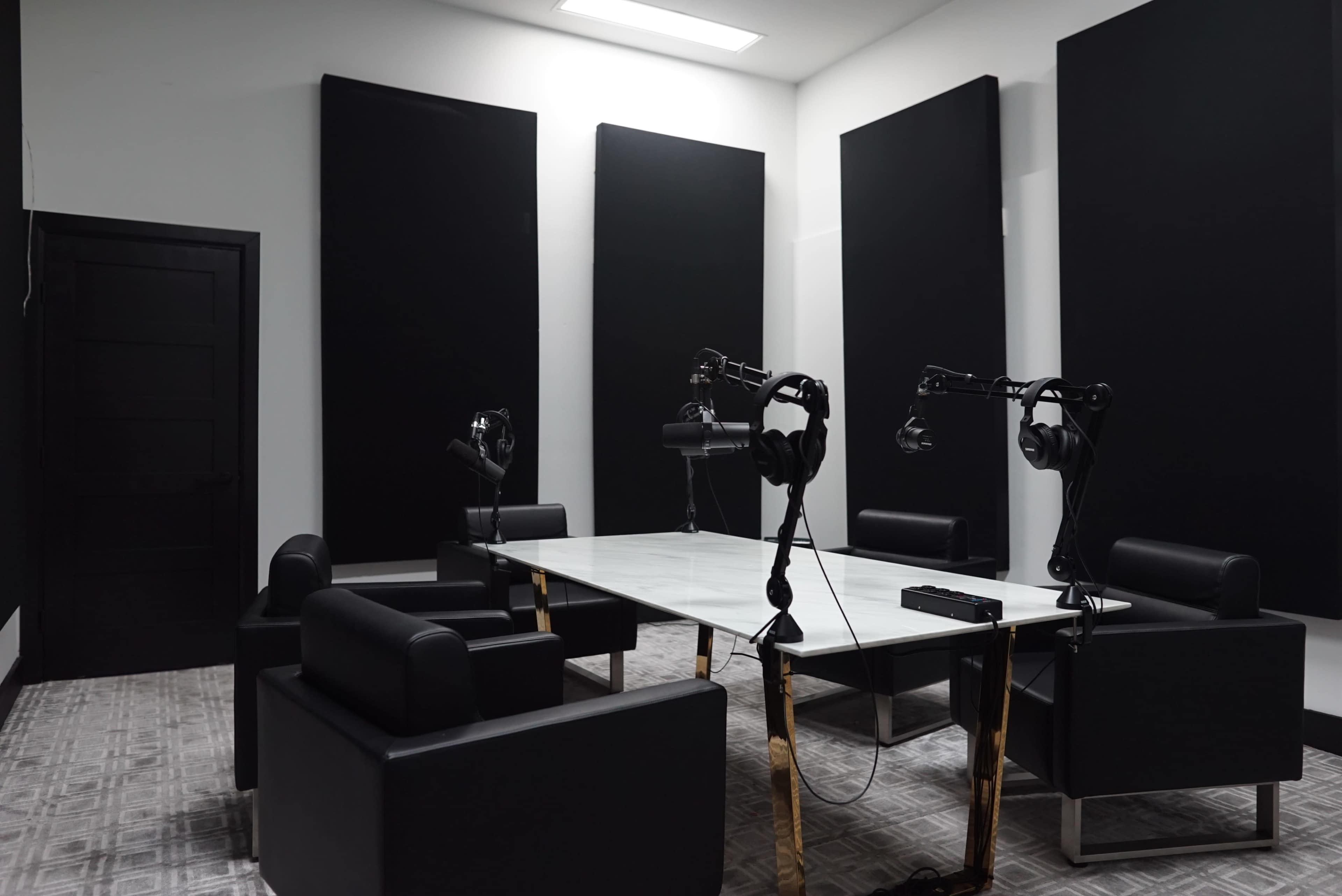 A soundproof room features a large marble table surrounded by black leather chairs and microphone setups.