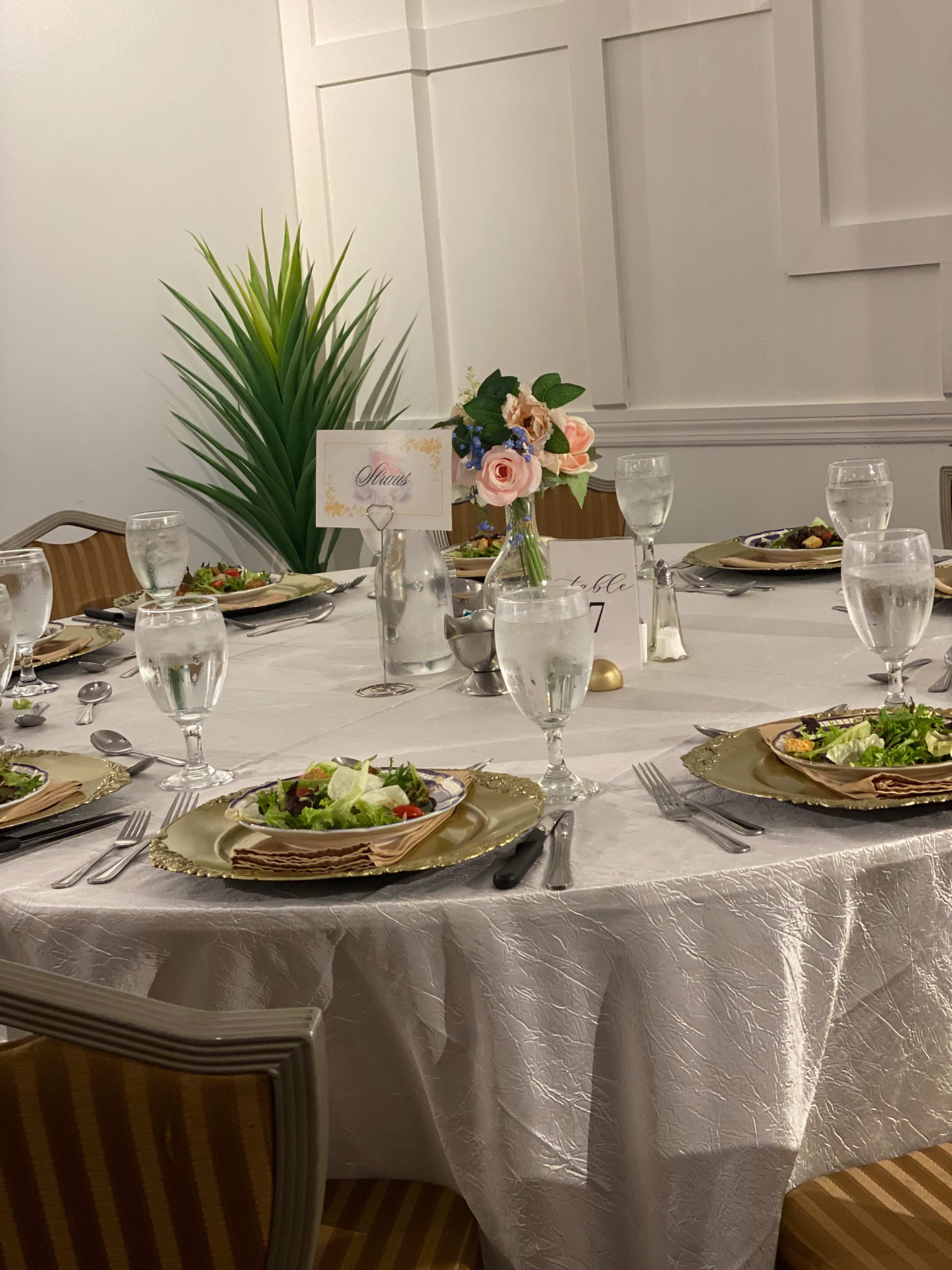 A dining table is elegantly set with plates of food, glasses of water, and a floral centerpiece, surrounded by striped chairs.
