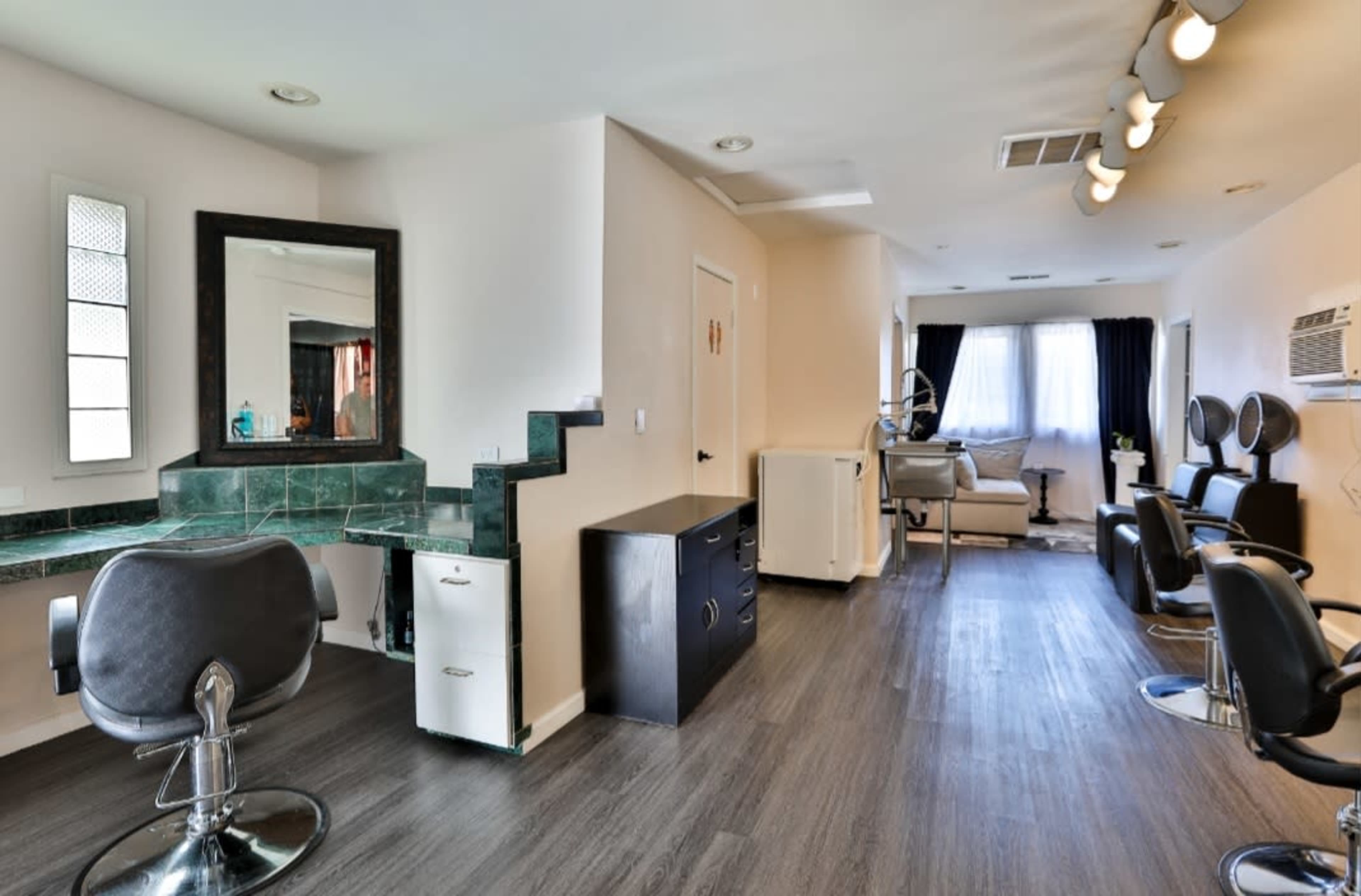 The image shows a modern hair salon featuring styling chairs, a reception area with a mirror, and a well-lit workspace.