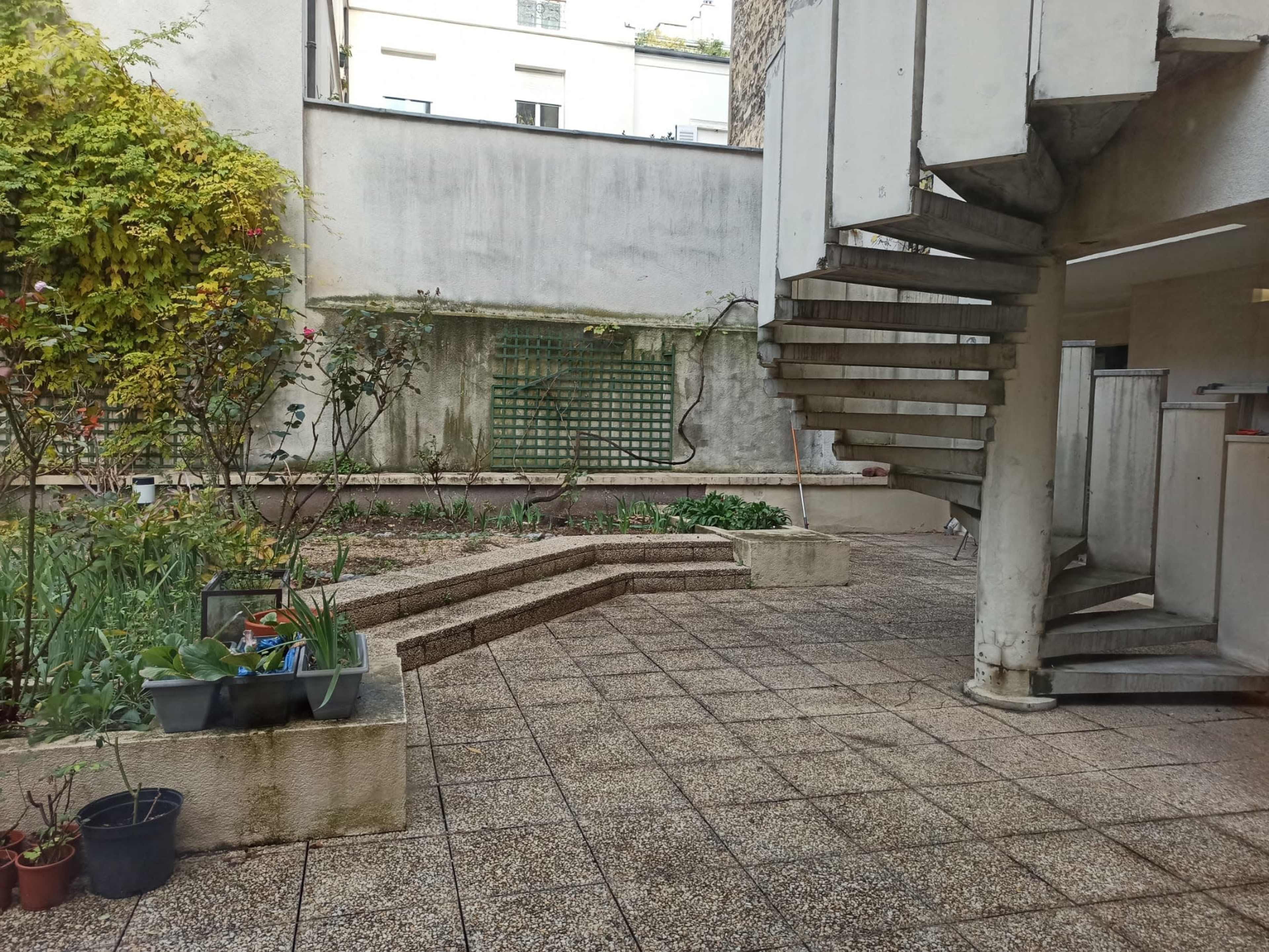 A small courtyard featuring a spiral staircase, flower beds, and a paved surface.