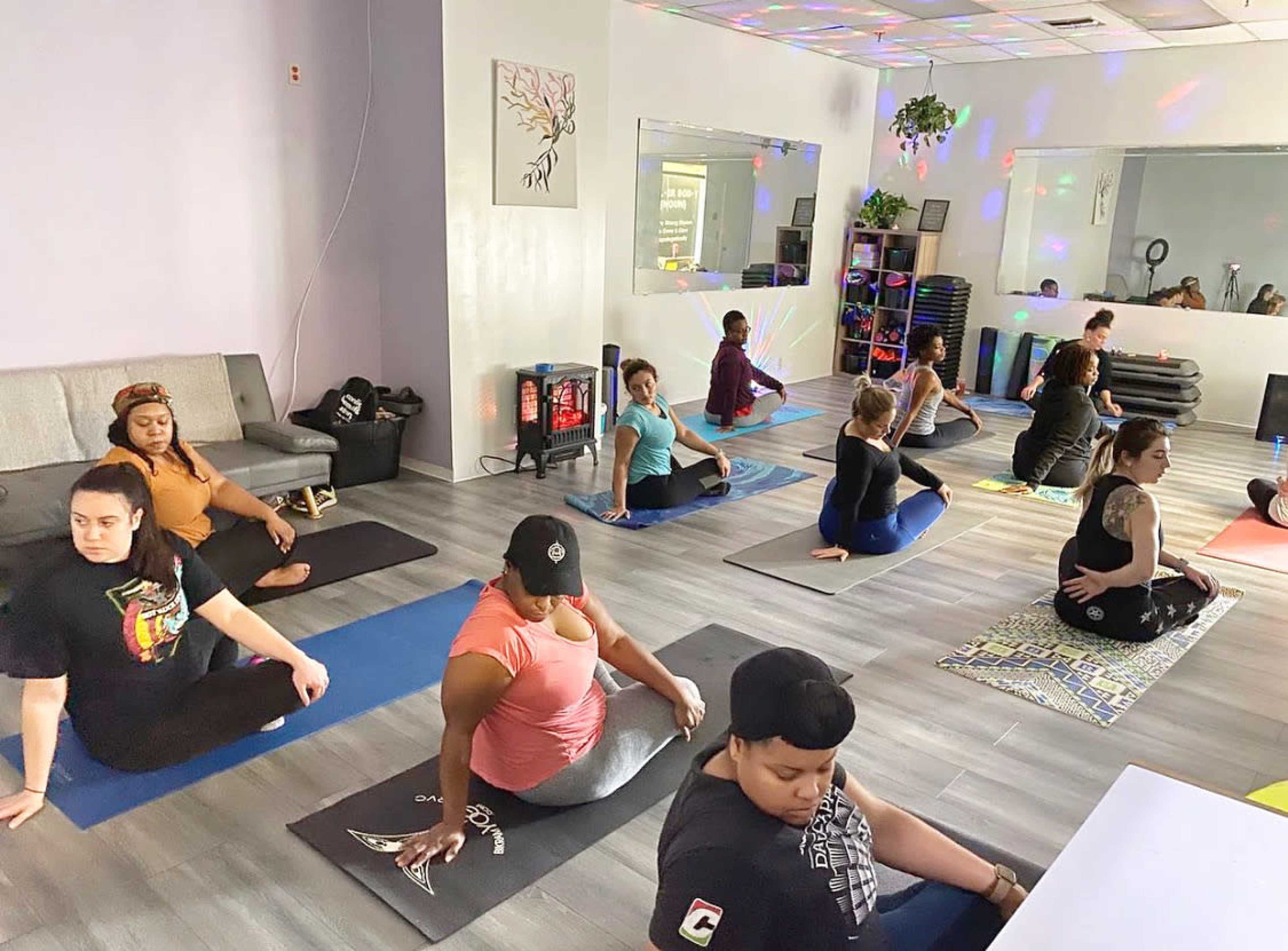 A group of individuals practices yoga in a studio with colorful lighting and yoga mats arranged on the floor.