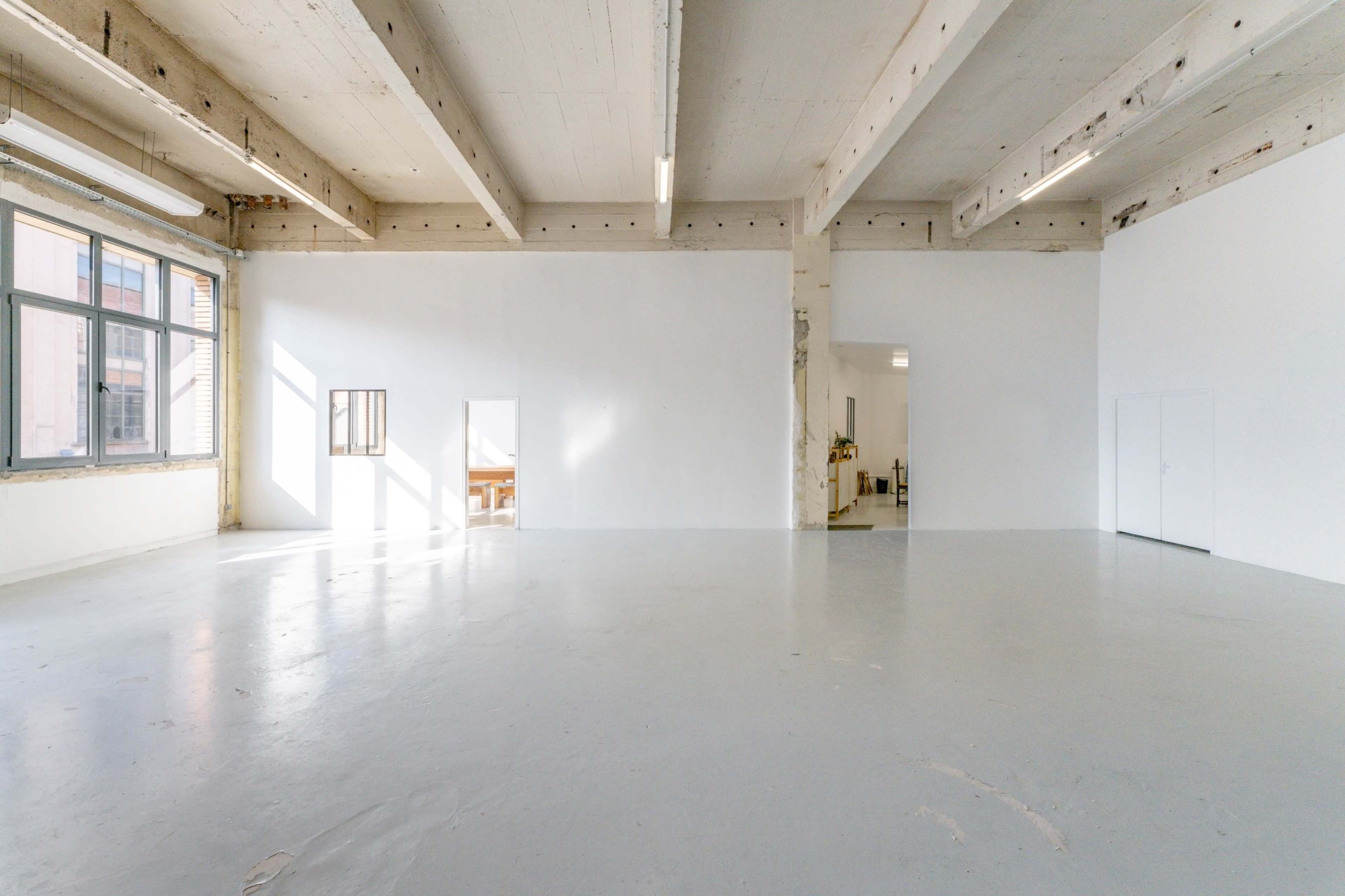 A spacious, empty industrial-style room with a polished concrete floor and large windows allowing natural light to enter.
