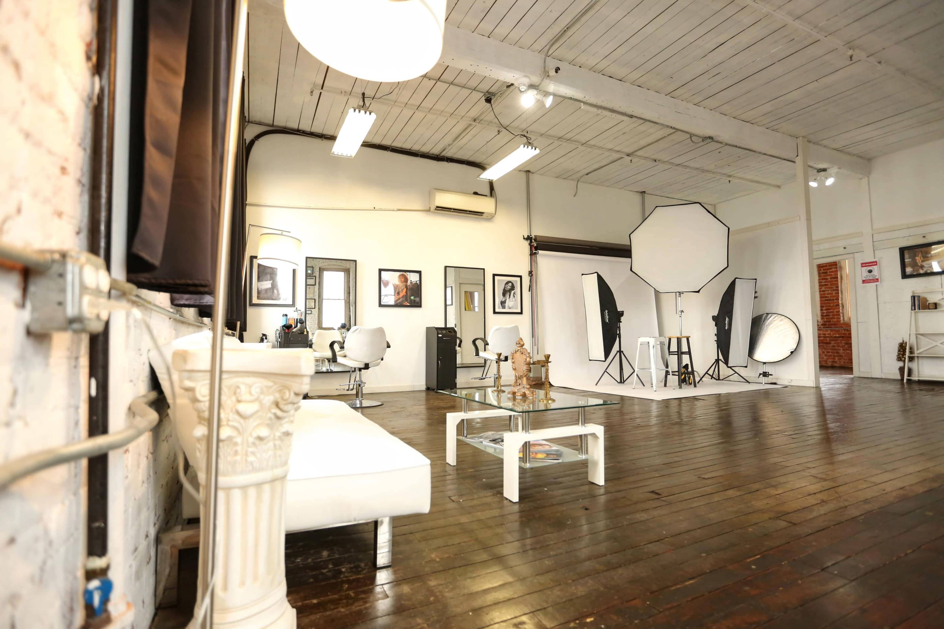 A spacious photography studio with wooden floors, white walls, and various lighting equipment arranged for a photo shoot.