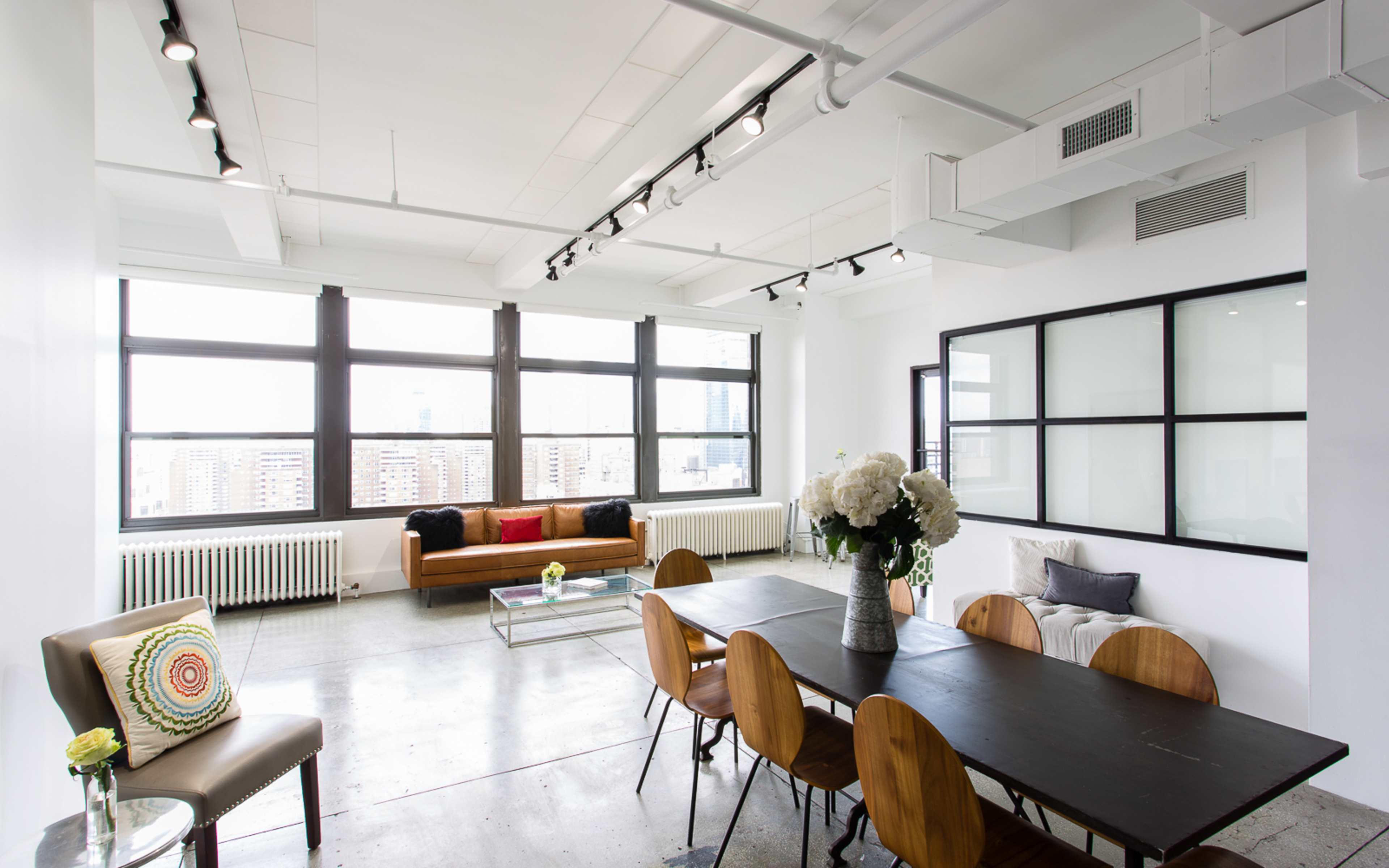 A modern, open-concept living space featuring a dining table, a sofa, and large windows that provide a view of the city.