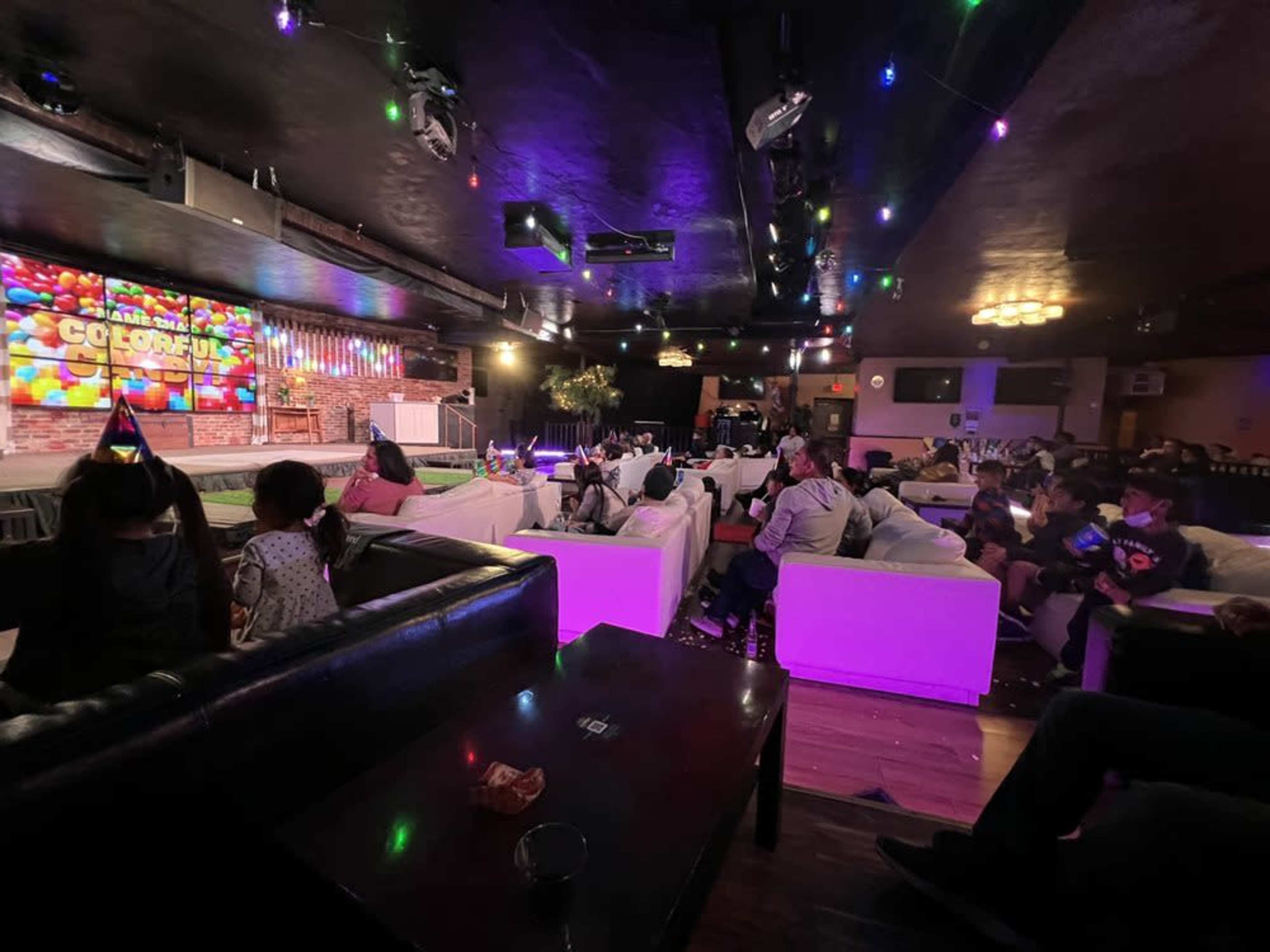 A lively lounge area with white couches, colorful lighting, and a large screen displaying the word "COLORFUL" while guests gather and socialize.