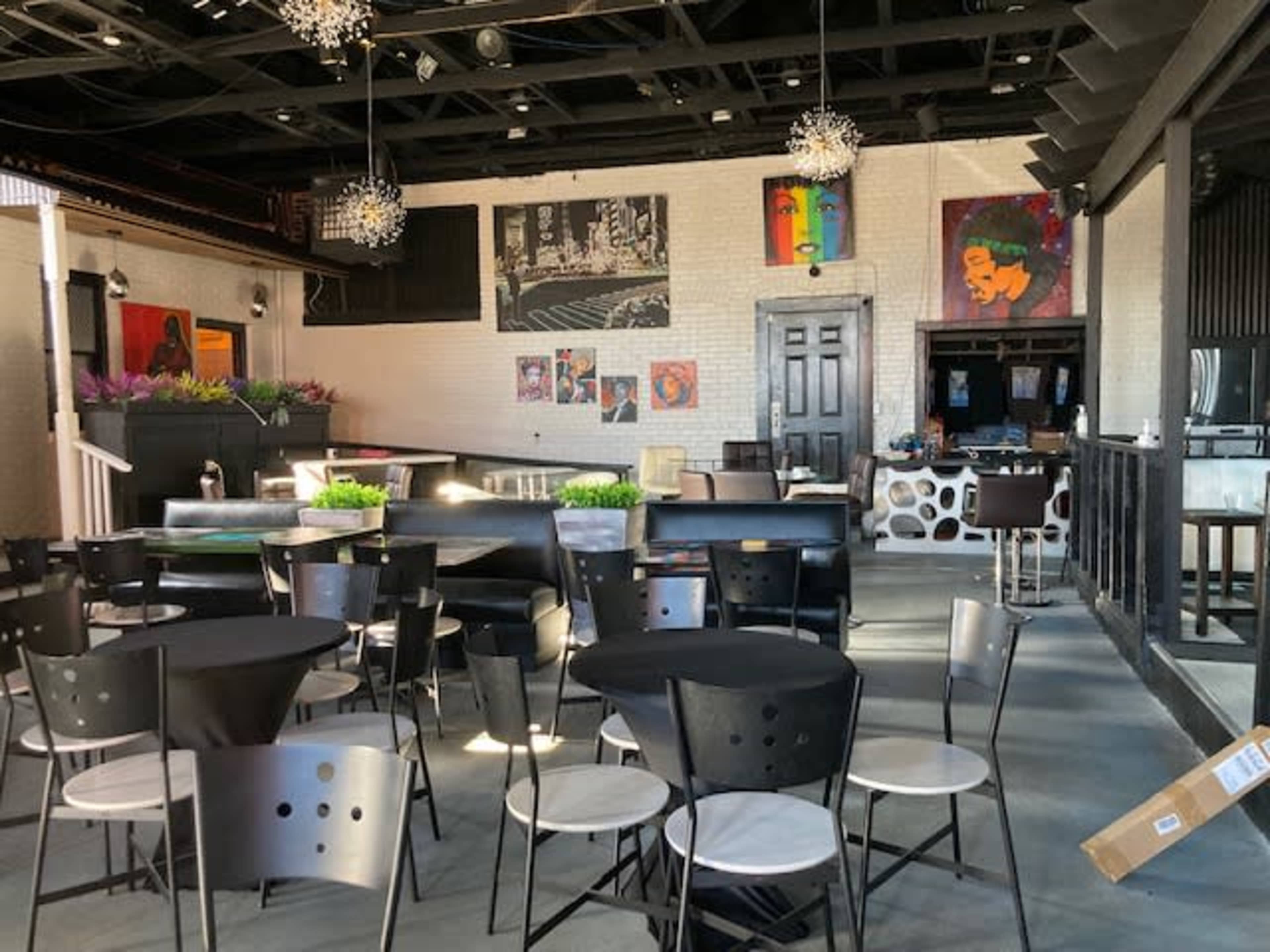 A spacious restaurant interior featuring black and white furniture, decorative wall art, and a bar area at the back.