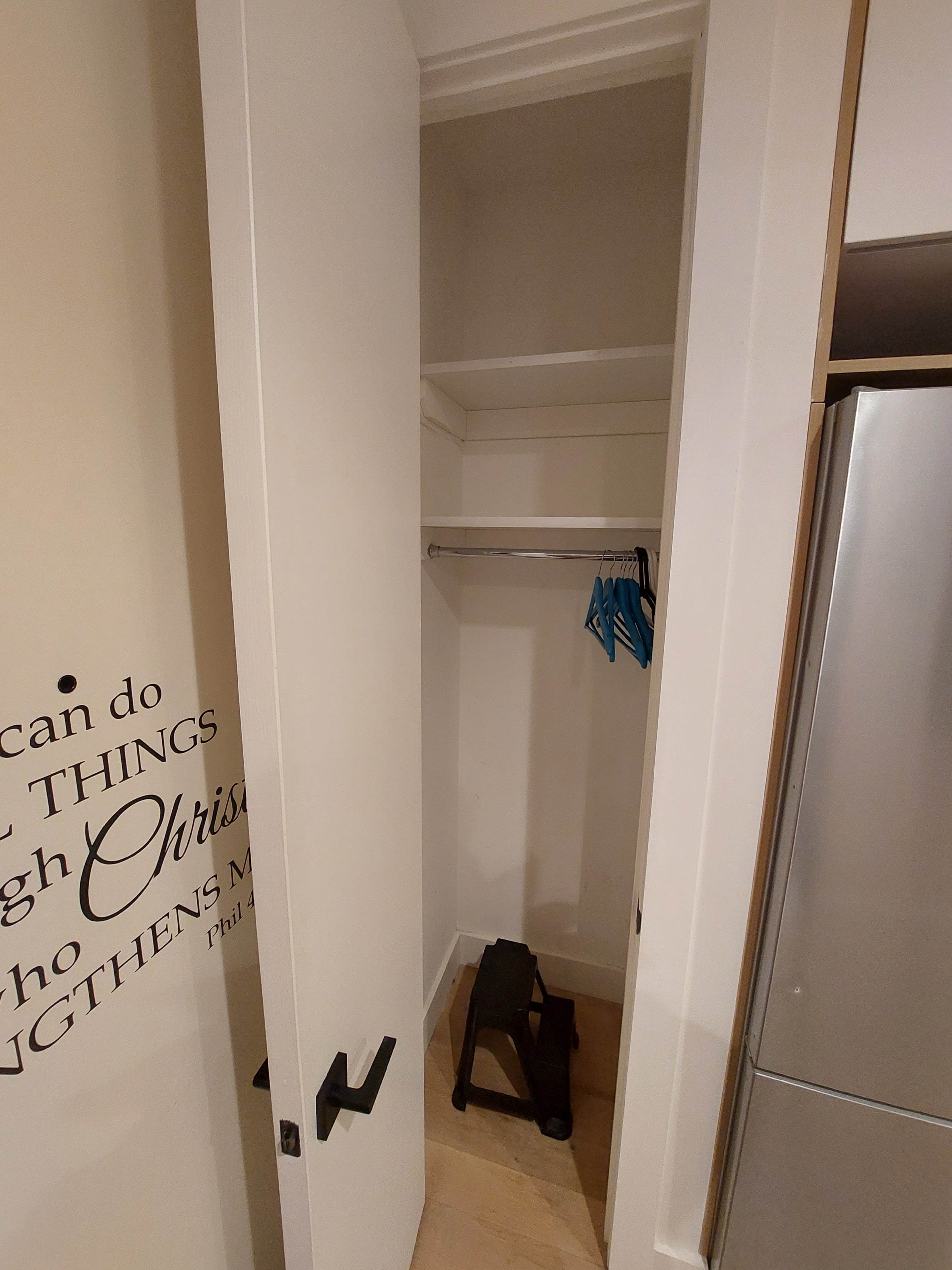 An empty closet with a small step stool and a few blue hangers on the top shelf.