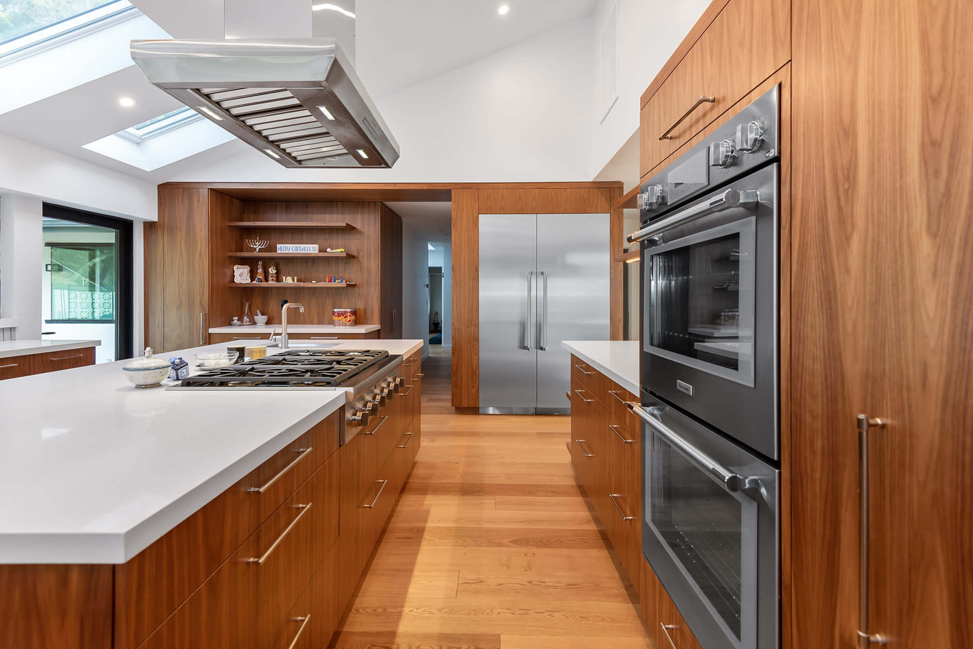 A modern kitchen featuring wooden cabinetry, a central island with a gas cooktop, and stainless steel appliances.