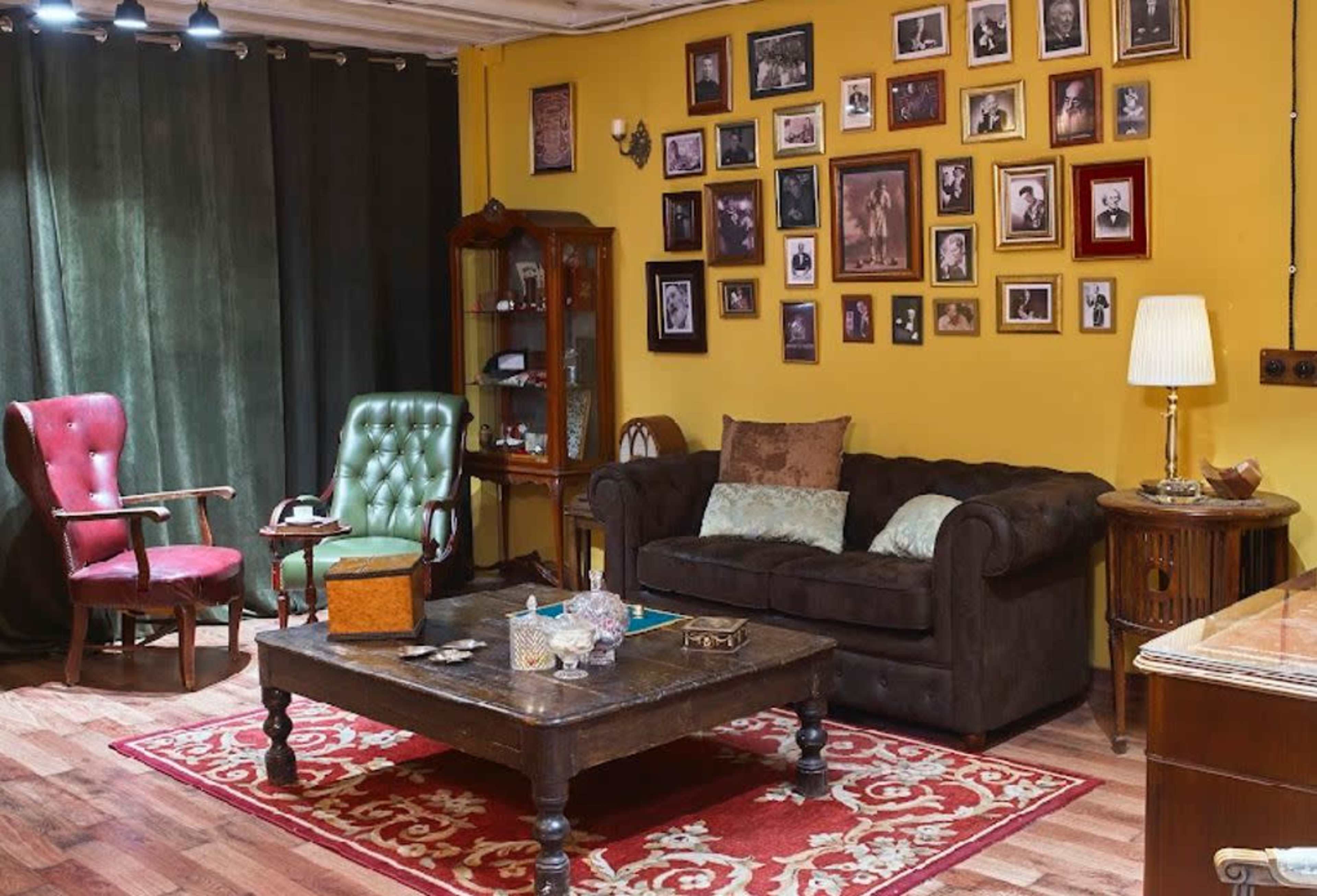 The image shows a cozy sitting area with a brown sofa, two armchairs, a wooden coffee table, and a wall adorned with various framed black-and-white photographs.