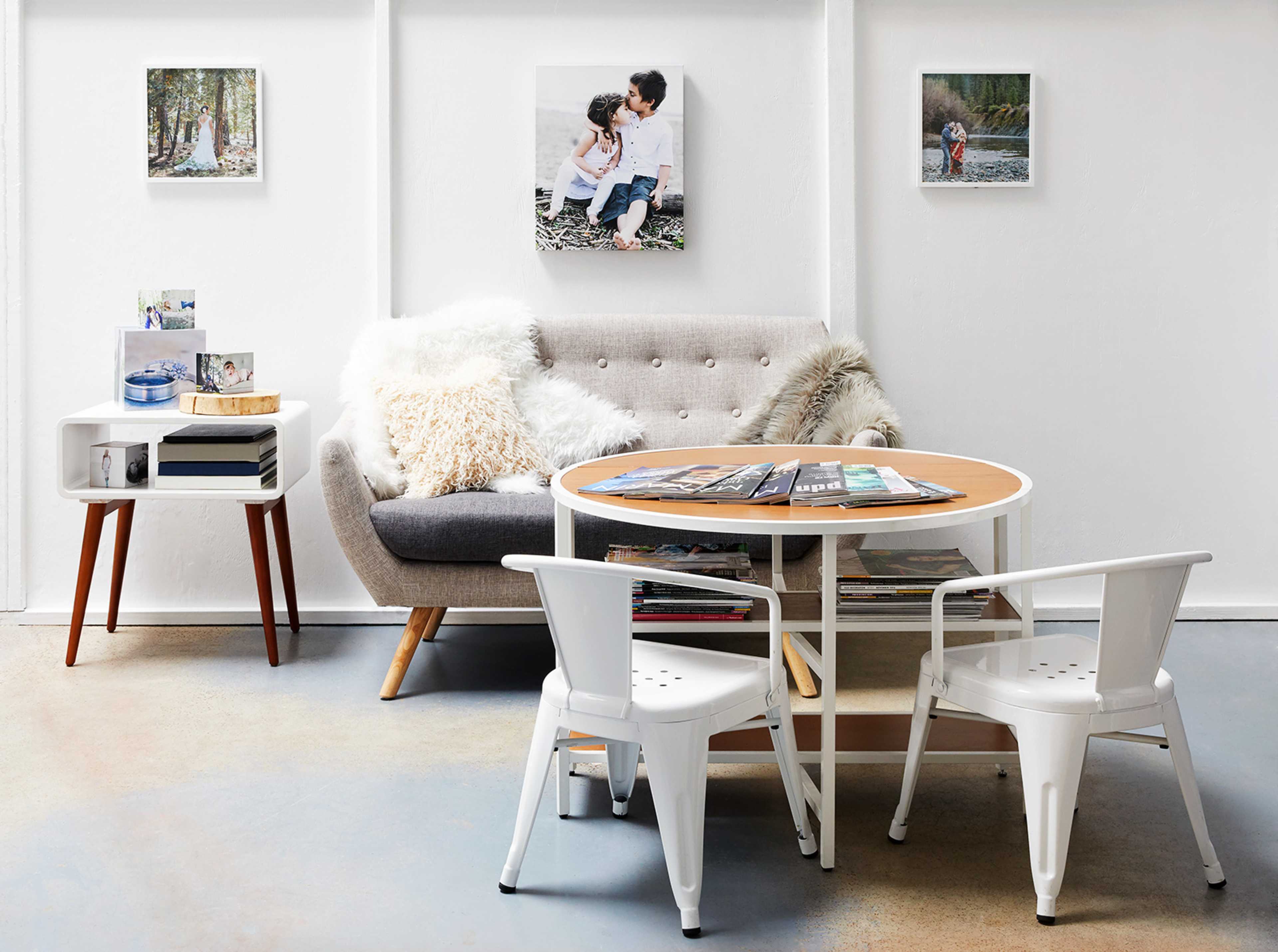 A modern living room with a grey sofa, a round wooden coffee table, and two white chairs, decorated with family photos on the walls.