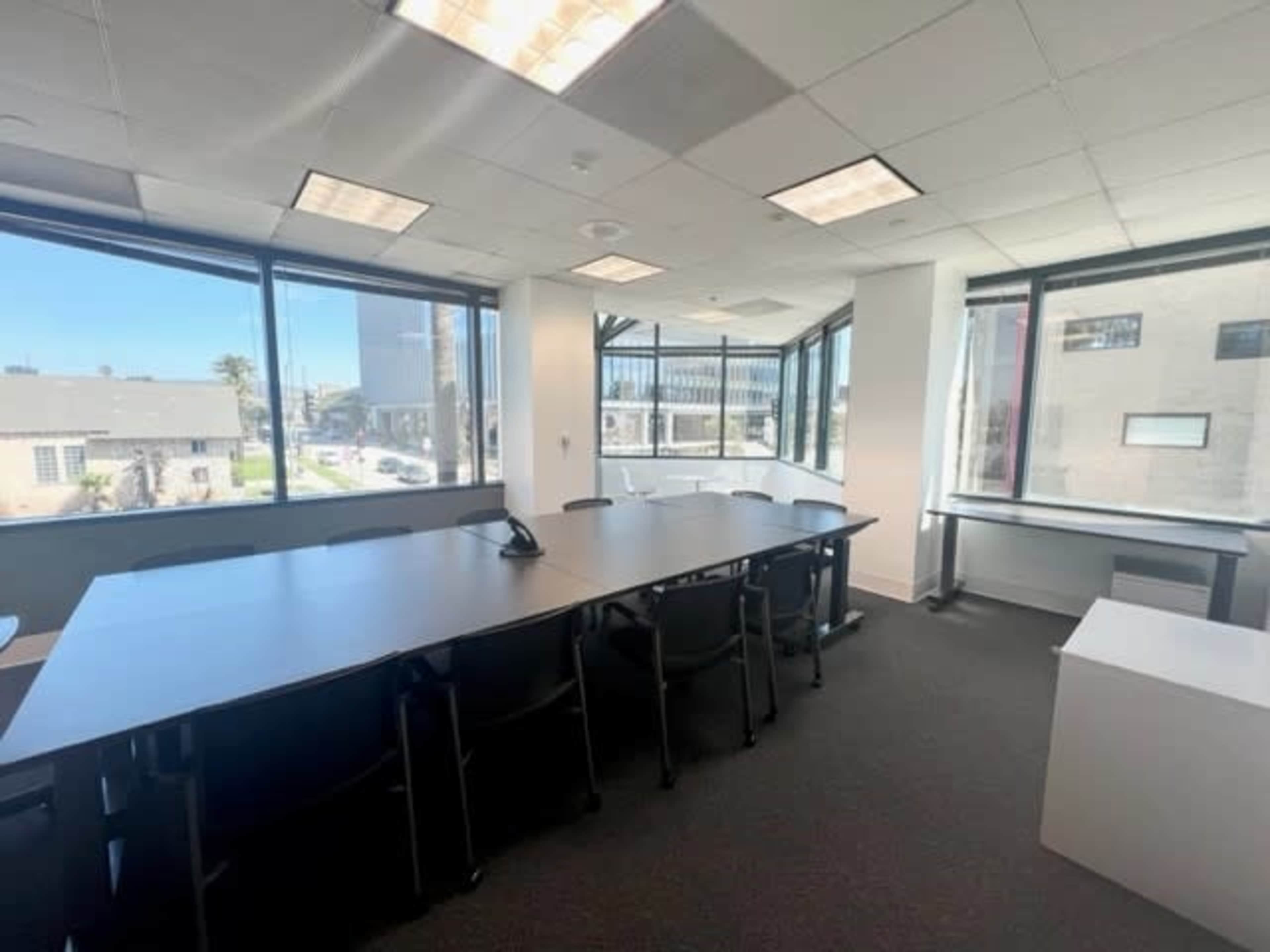 A modern conference room features a large table surrounded by chairs and large windows offering a view of an outdoor area.