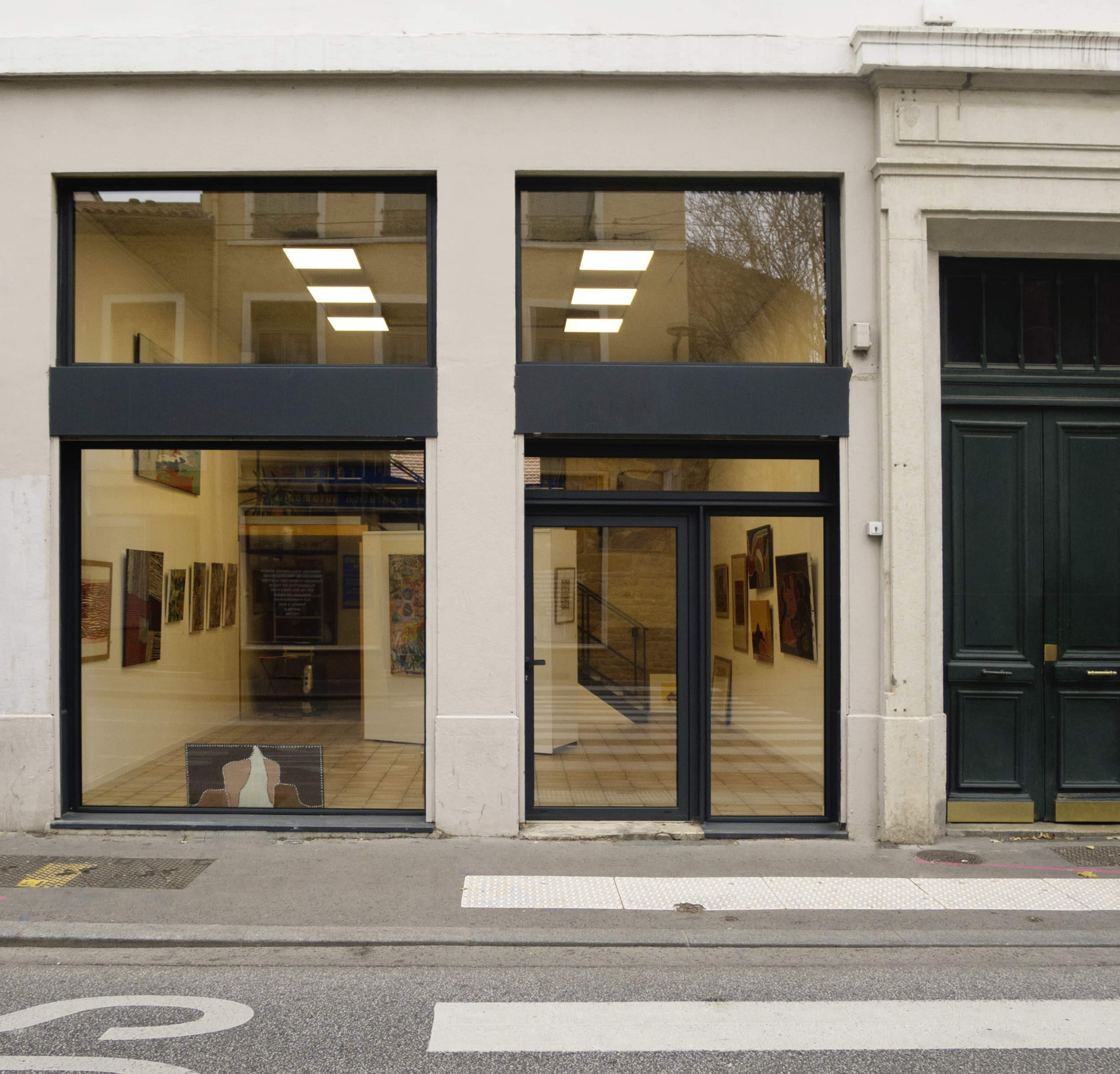 The image shows a storefront with large glass windows displaying an art gallery's interior, featuring framed artworks on the walls.