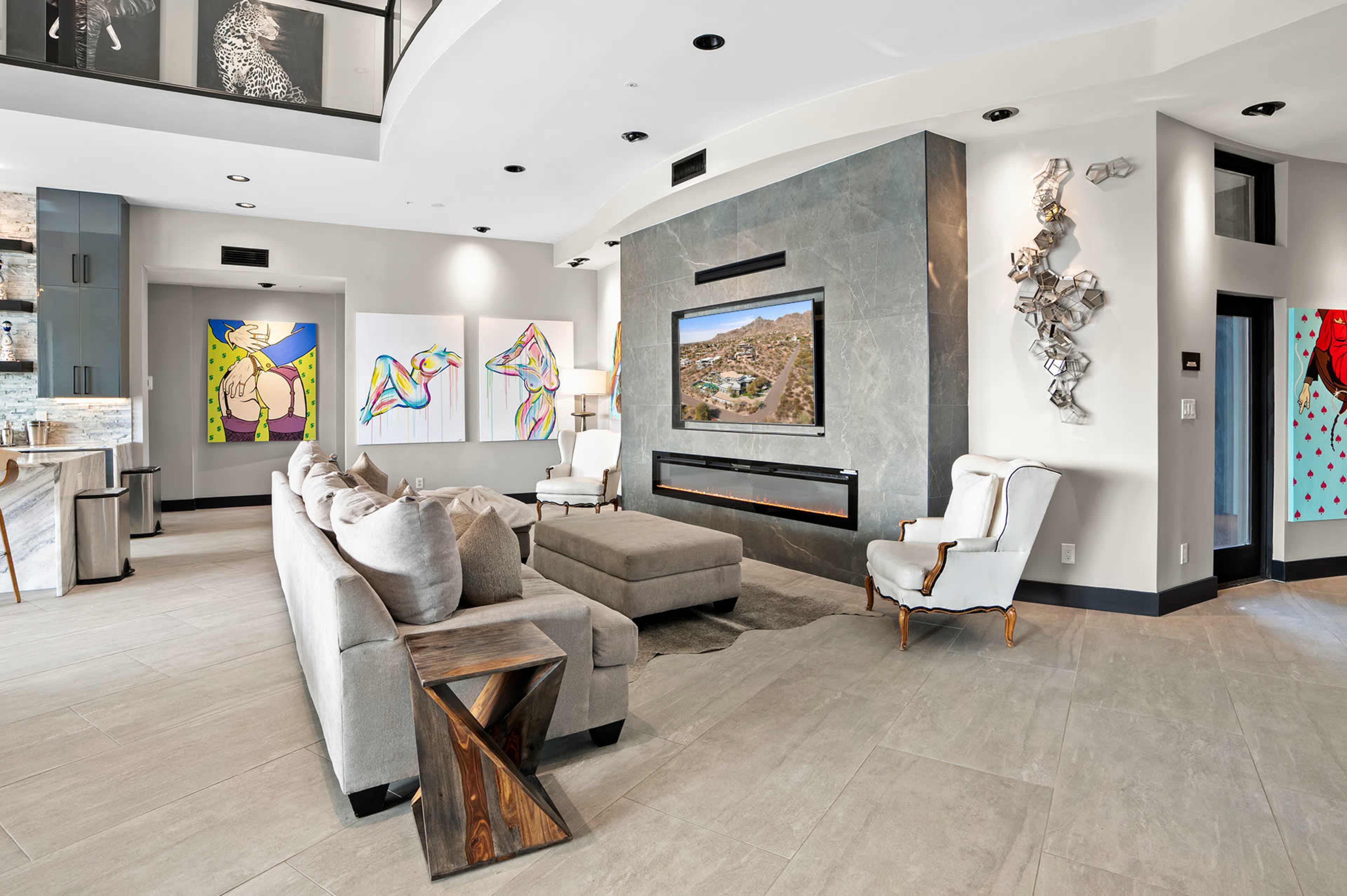 The image shows a modern living room with a sectional sofa, an entertainment unit with a television, and colorful artwork on the walls.
