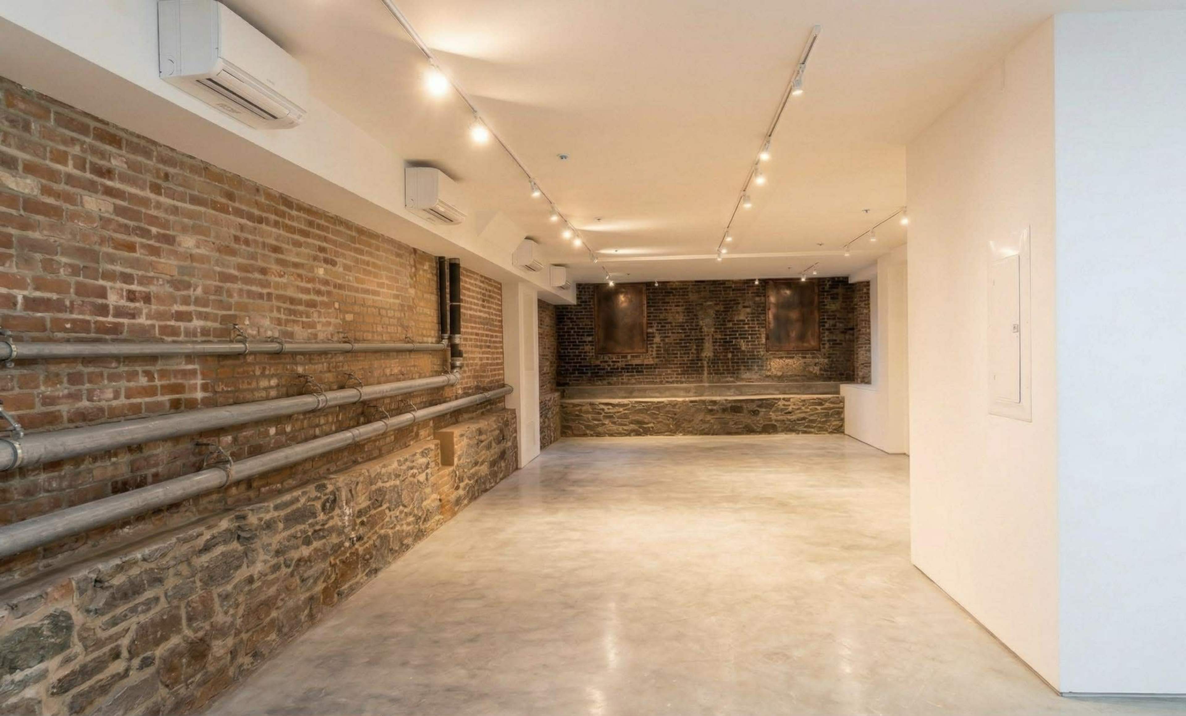 The image shows a spacious interior with exposed brick walls, polished concrete flooring, and industrial-style lighting.