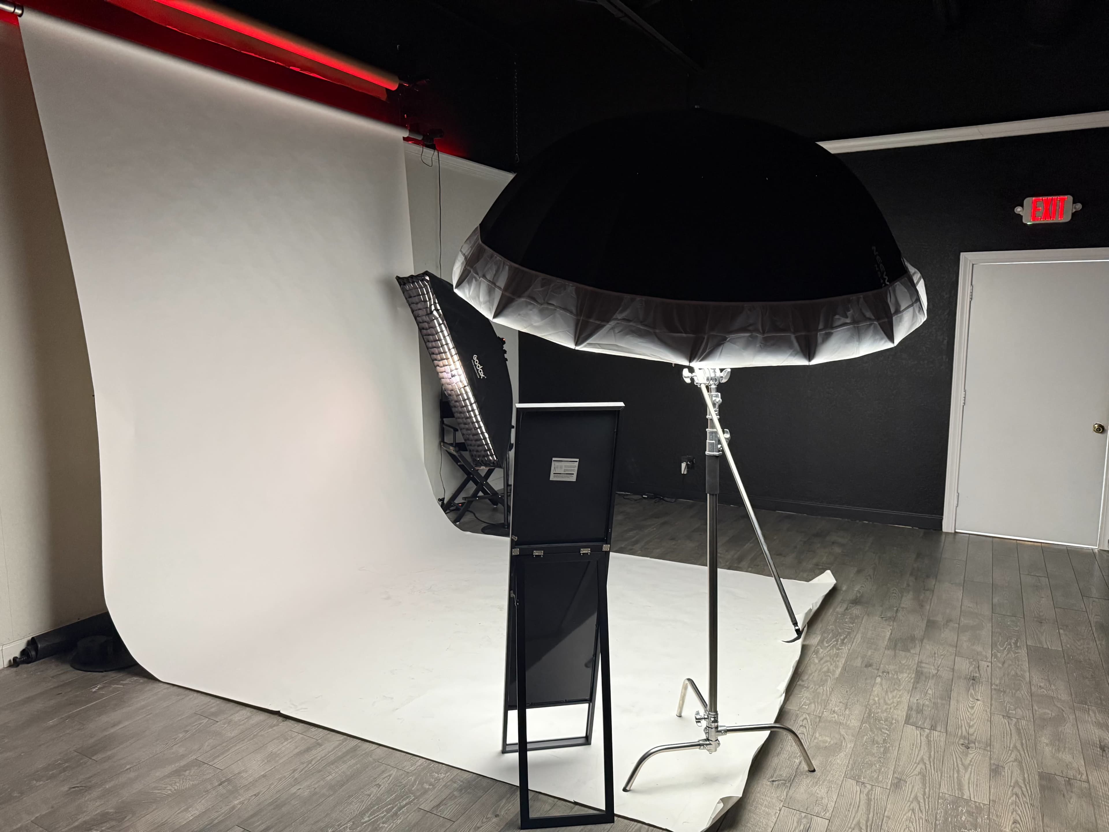 The image shows a photography studio setup featuring a backdrop, softbox light, and a chair.
