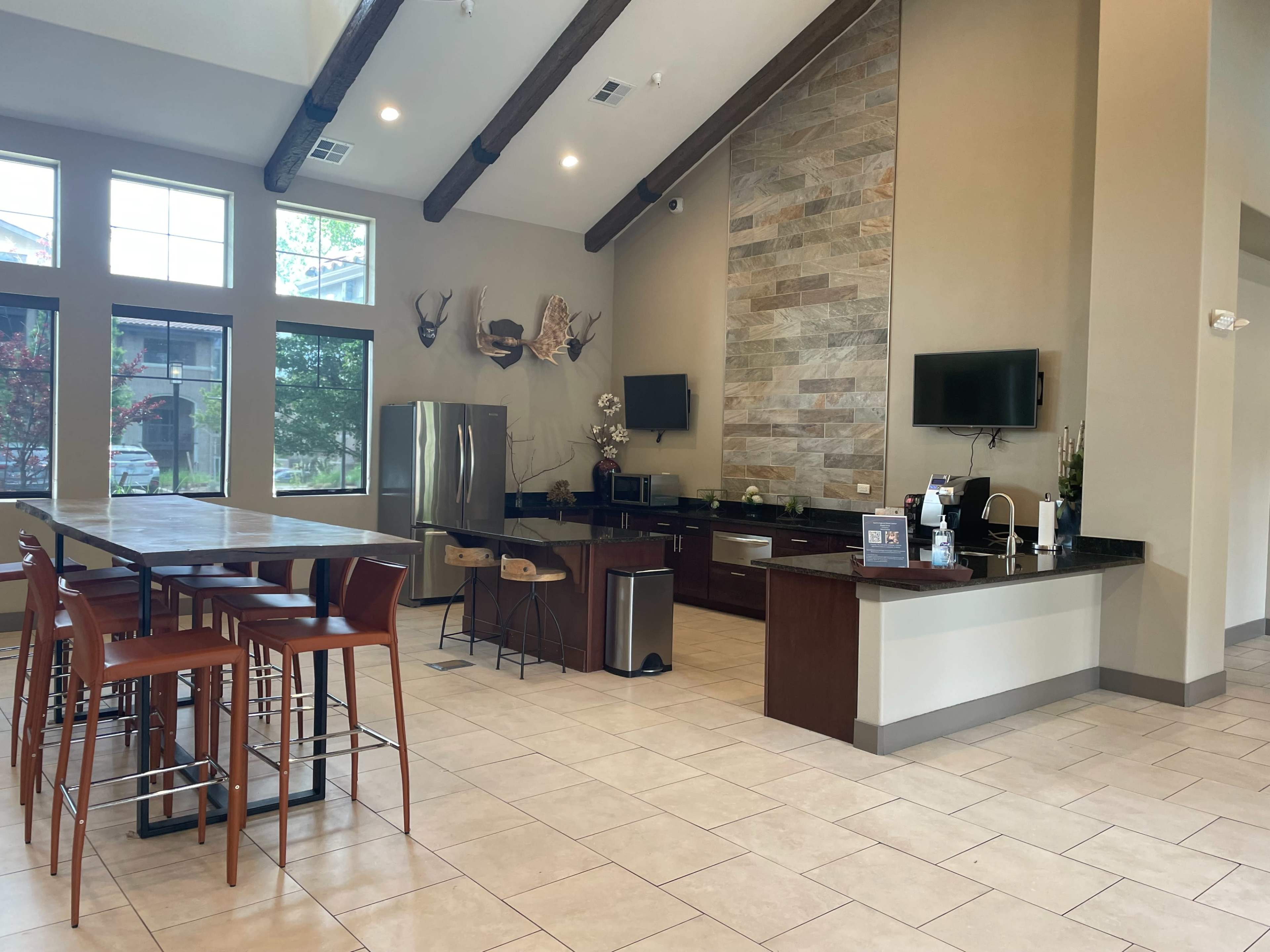 The image shows a modern kitchen and dining area with a large table, bar stools, a refrigerator, and a stone accent wall.