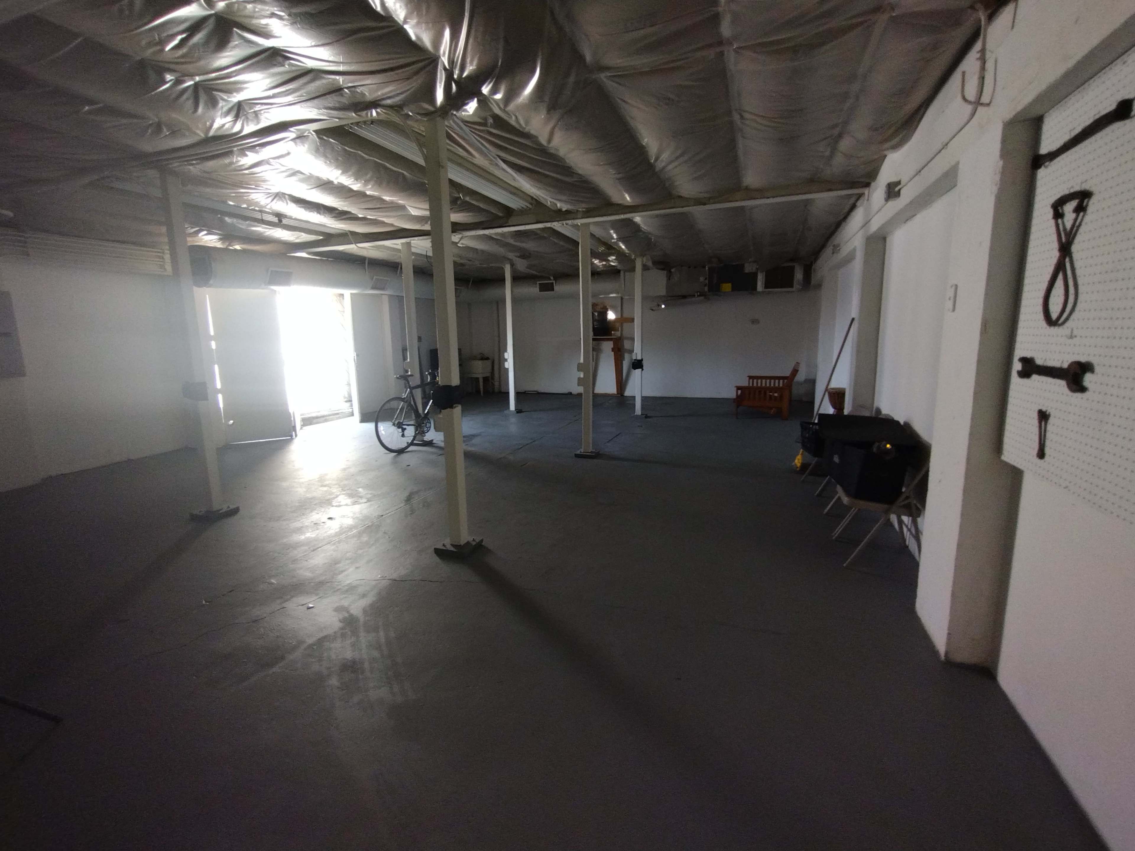 An empty garage or storage space with concrete flooring, exposed beams, and a bicycle leaning against a support column.