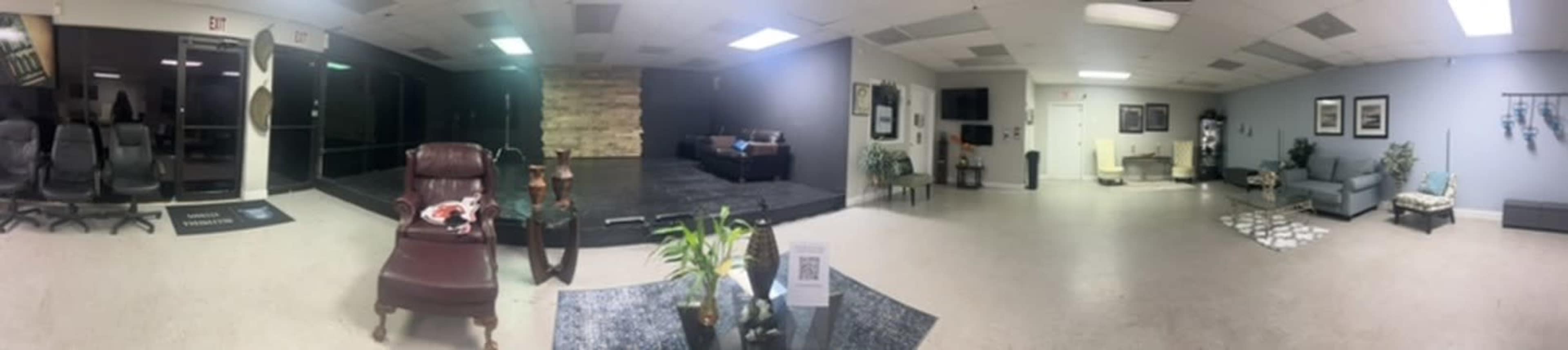 The image shows a spacious interior with a seating area, performance stage, and decorative plants.