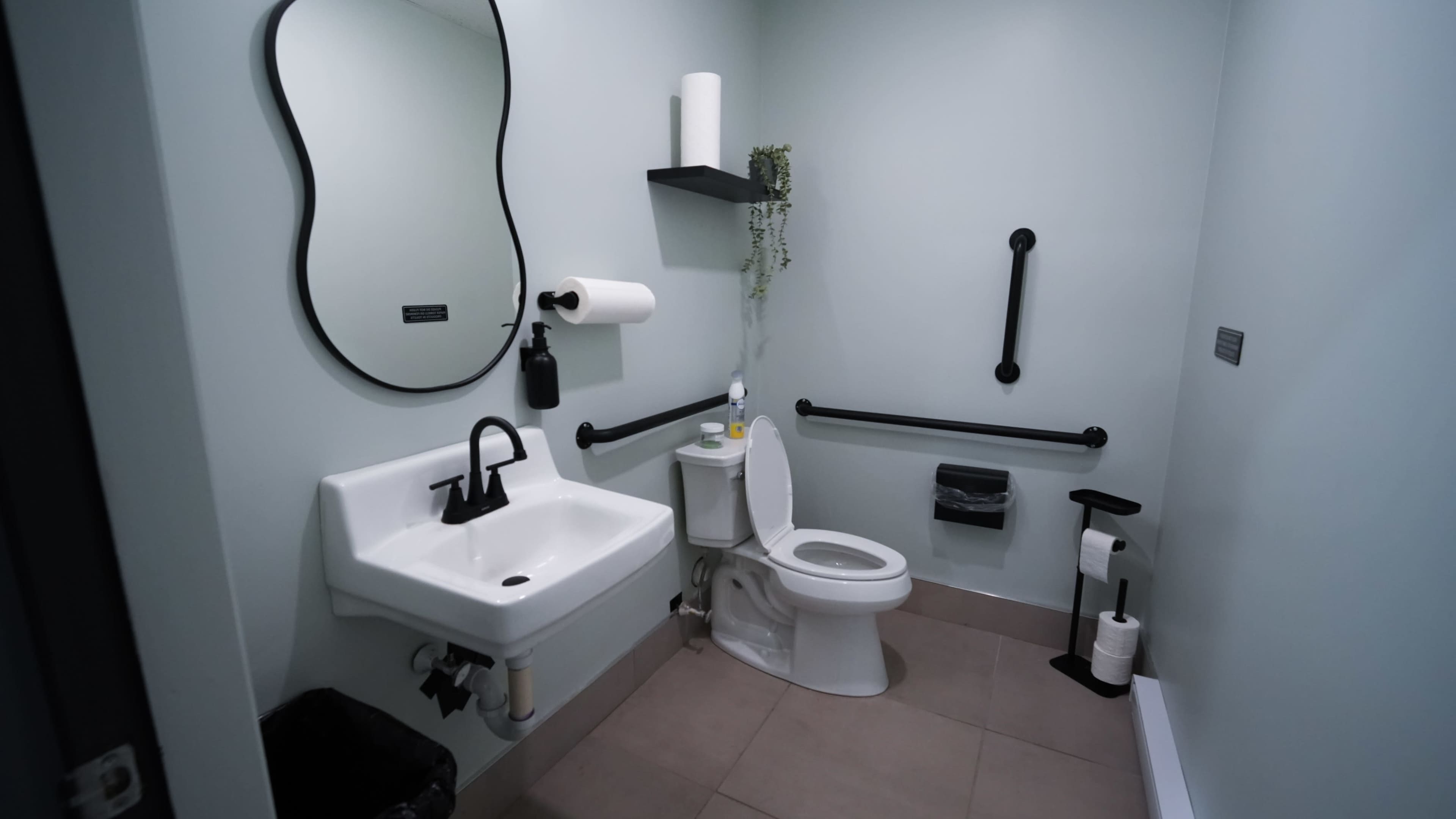 The image shows a small, modern bathroom with a sink, toilet, and various accessories against a light green wall.