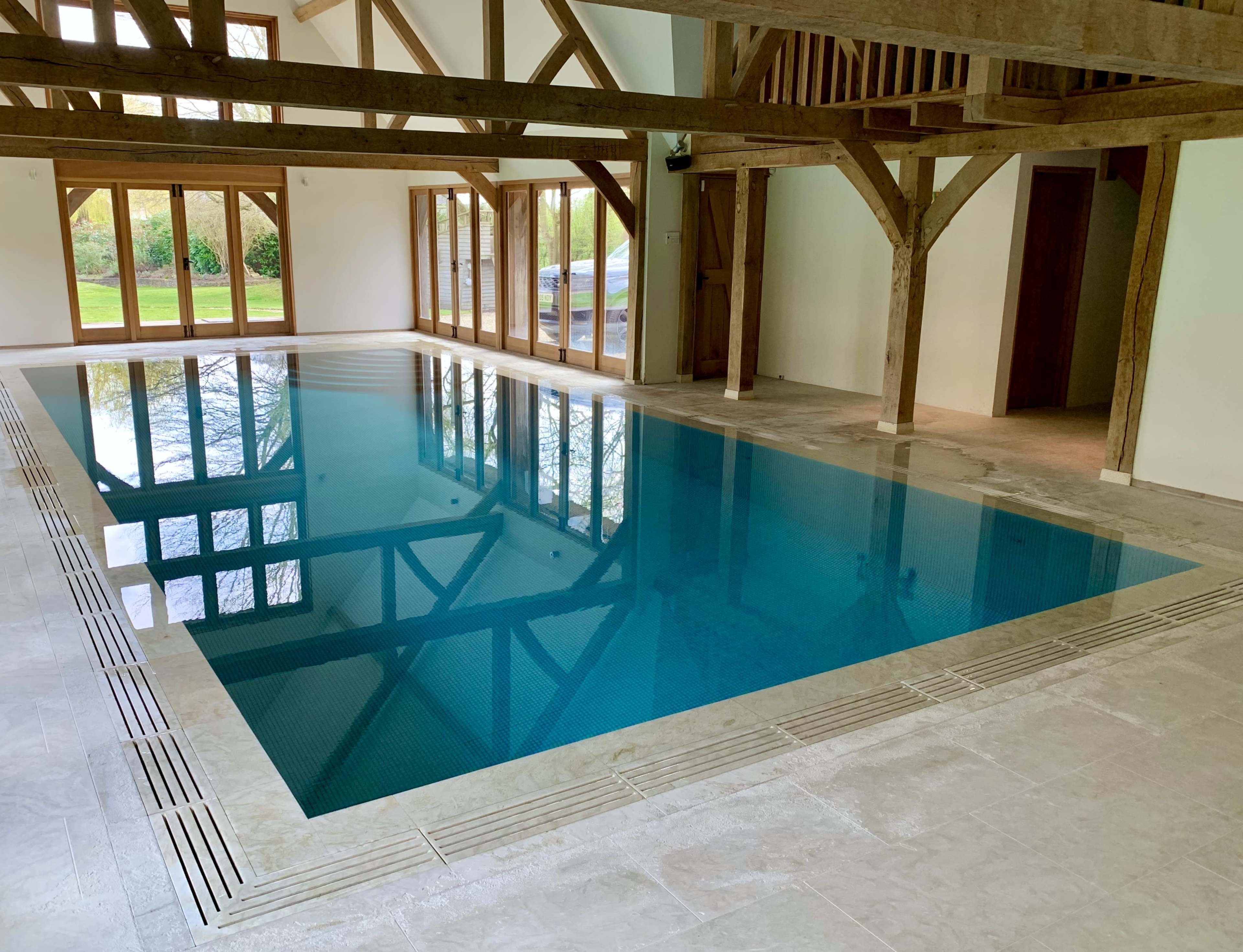 An indoor swimming pool with wooden beams and large windows allowing natural light to illuminate the space.