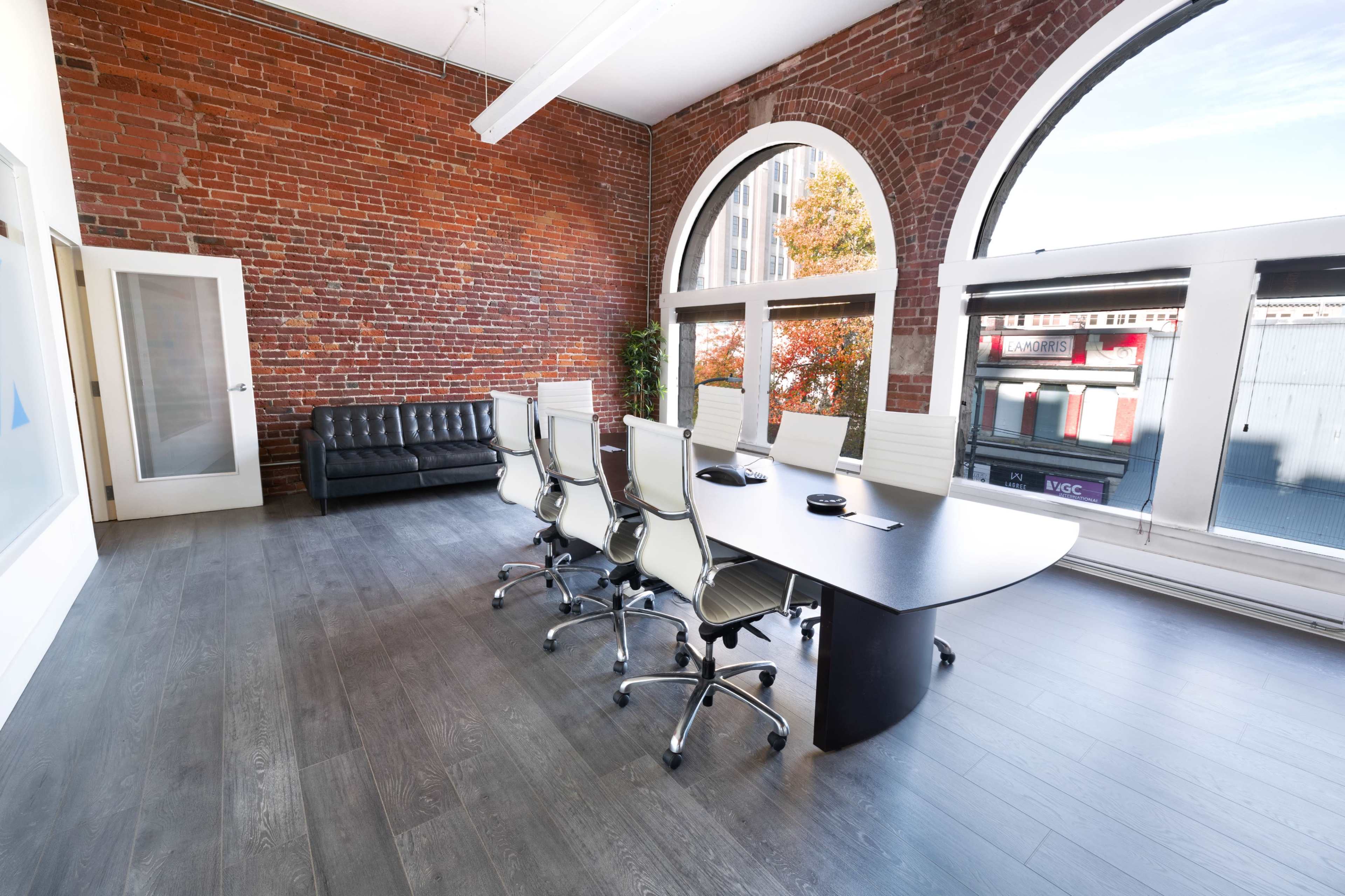A modern conference room with a large table, ergonomic chairs, a leather sofa, and exposed brick walls.