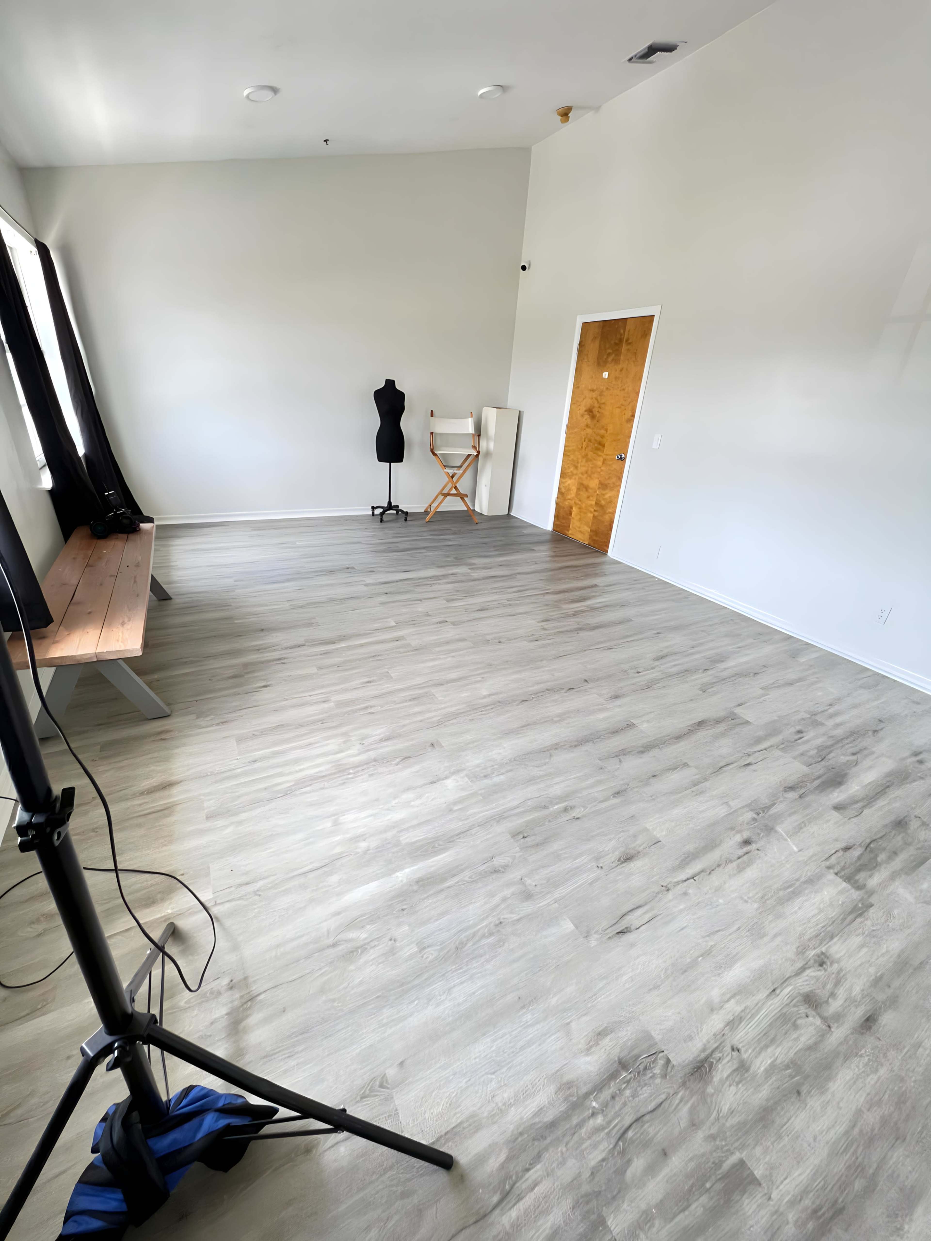 The image shows an empty room with light-colored wooden flooring, a bench against one wall, and a dressmaker's mannequin in the corner.