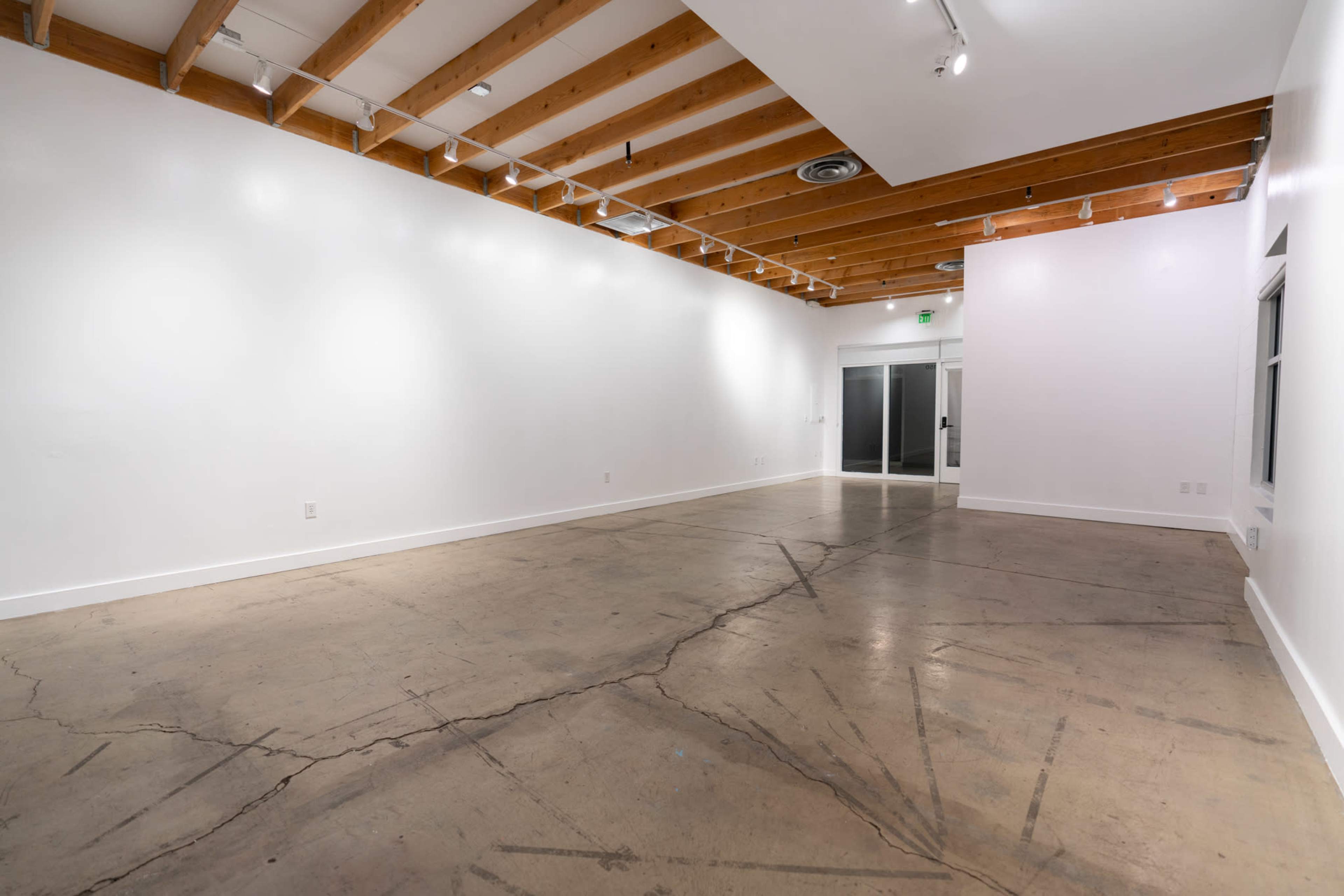 A spacious, empty room with concrete flooring and exposed wooden beams on the ceiling.