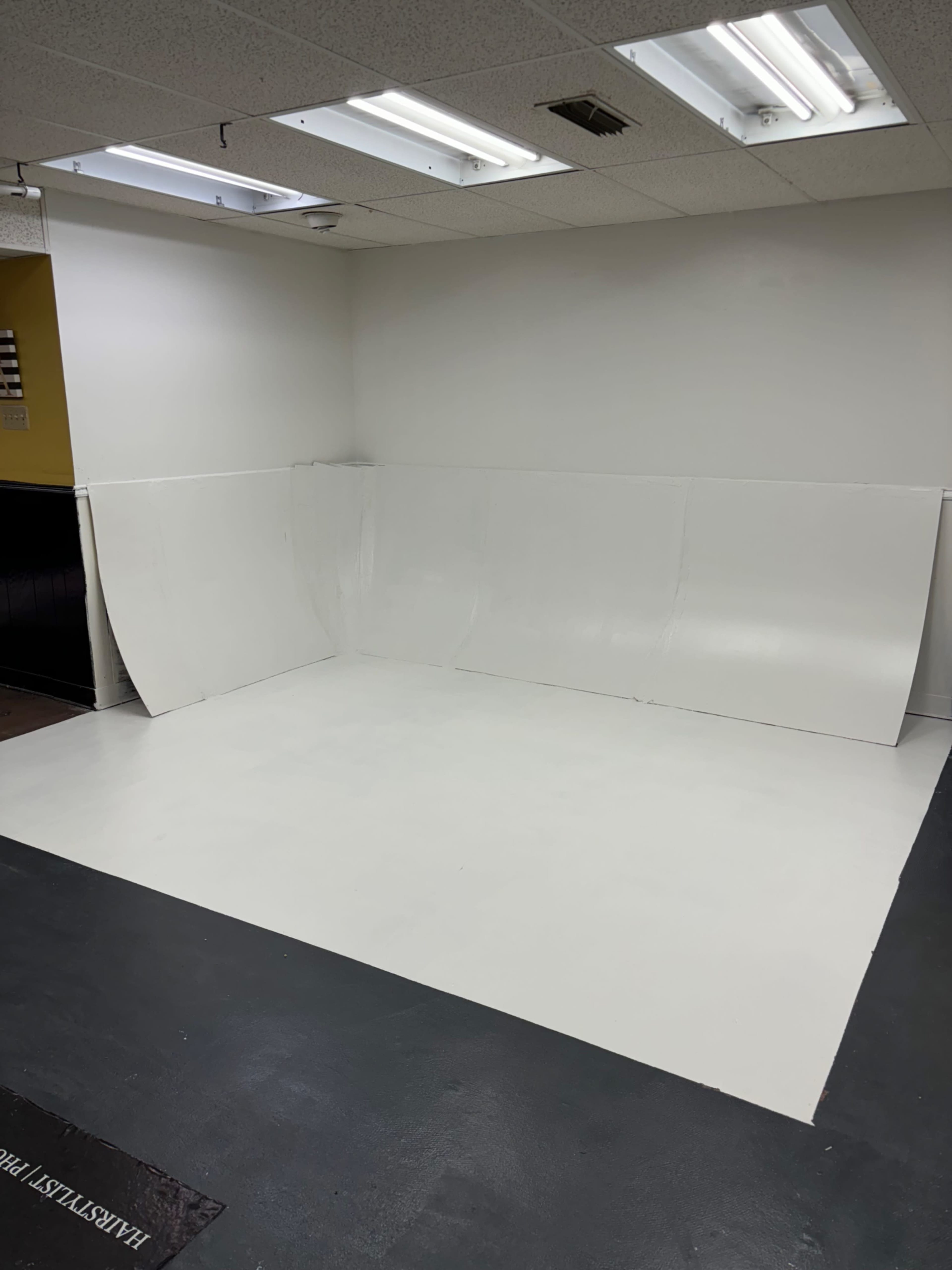 The image shows a blank, white studio space with a seamless background and a clean floor, suitable for photography or filming.