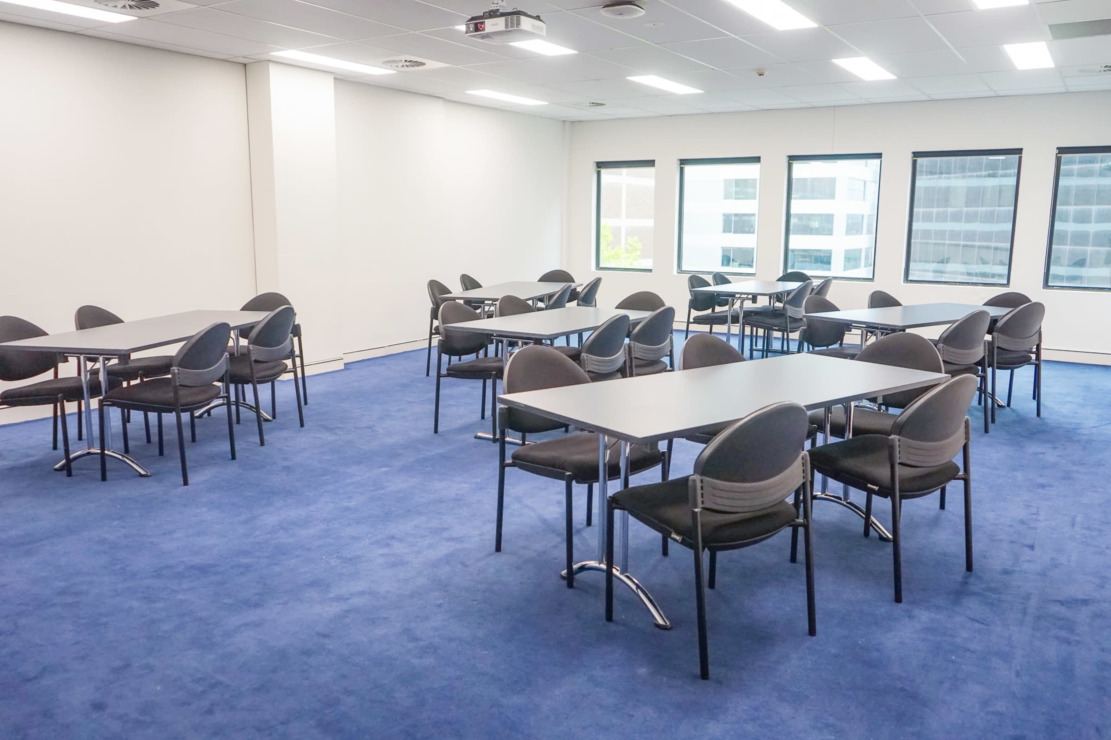 A conference room set up with several tables and chairs on a blue carpet.
