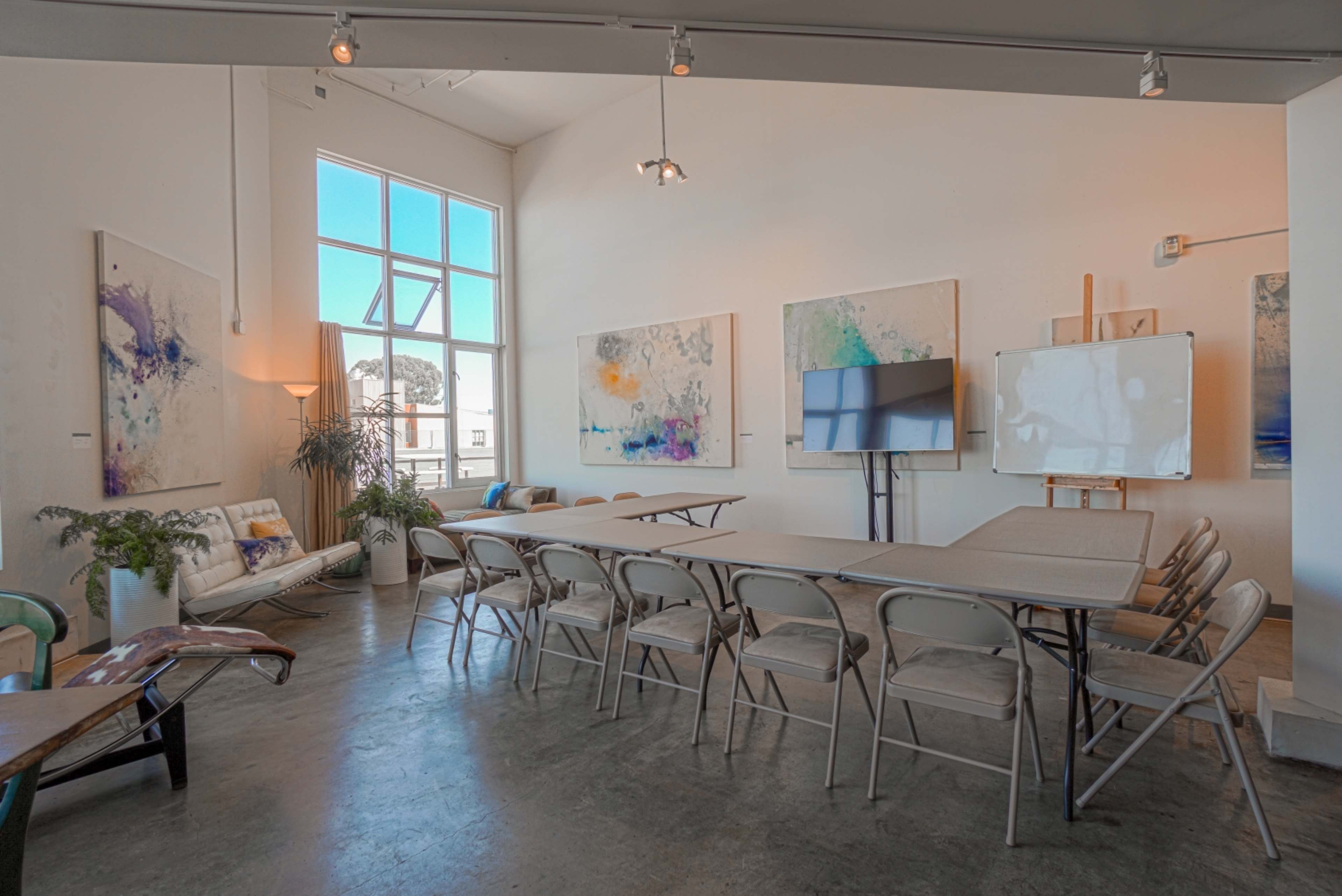 A spacious meeting room with a large table surrounded by folding chairs, decorative artwork on the walls, and large windows allowing natural light.