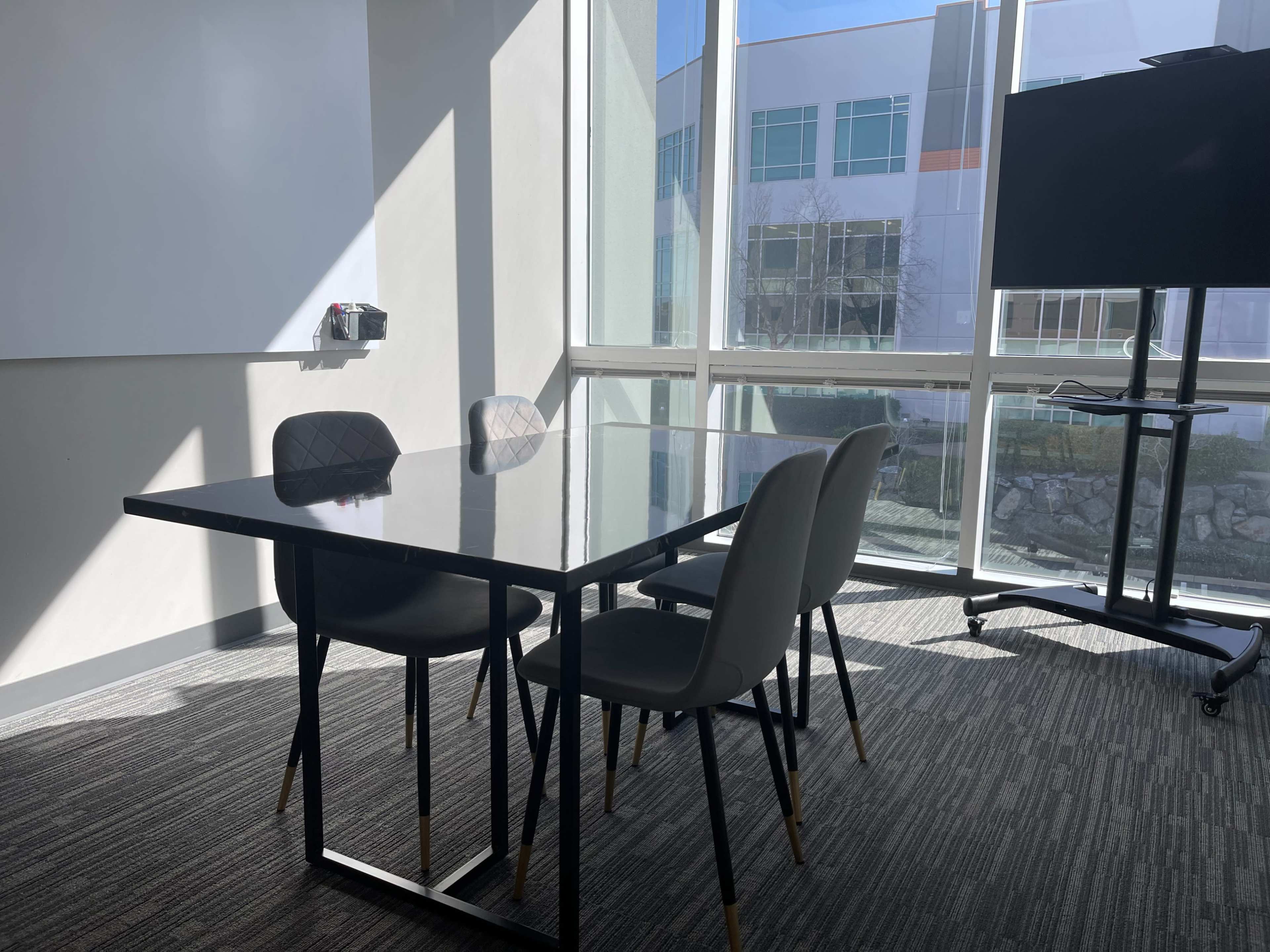 A conference room with a black table and four chairs is illuminated by natural light from the windows.