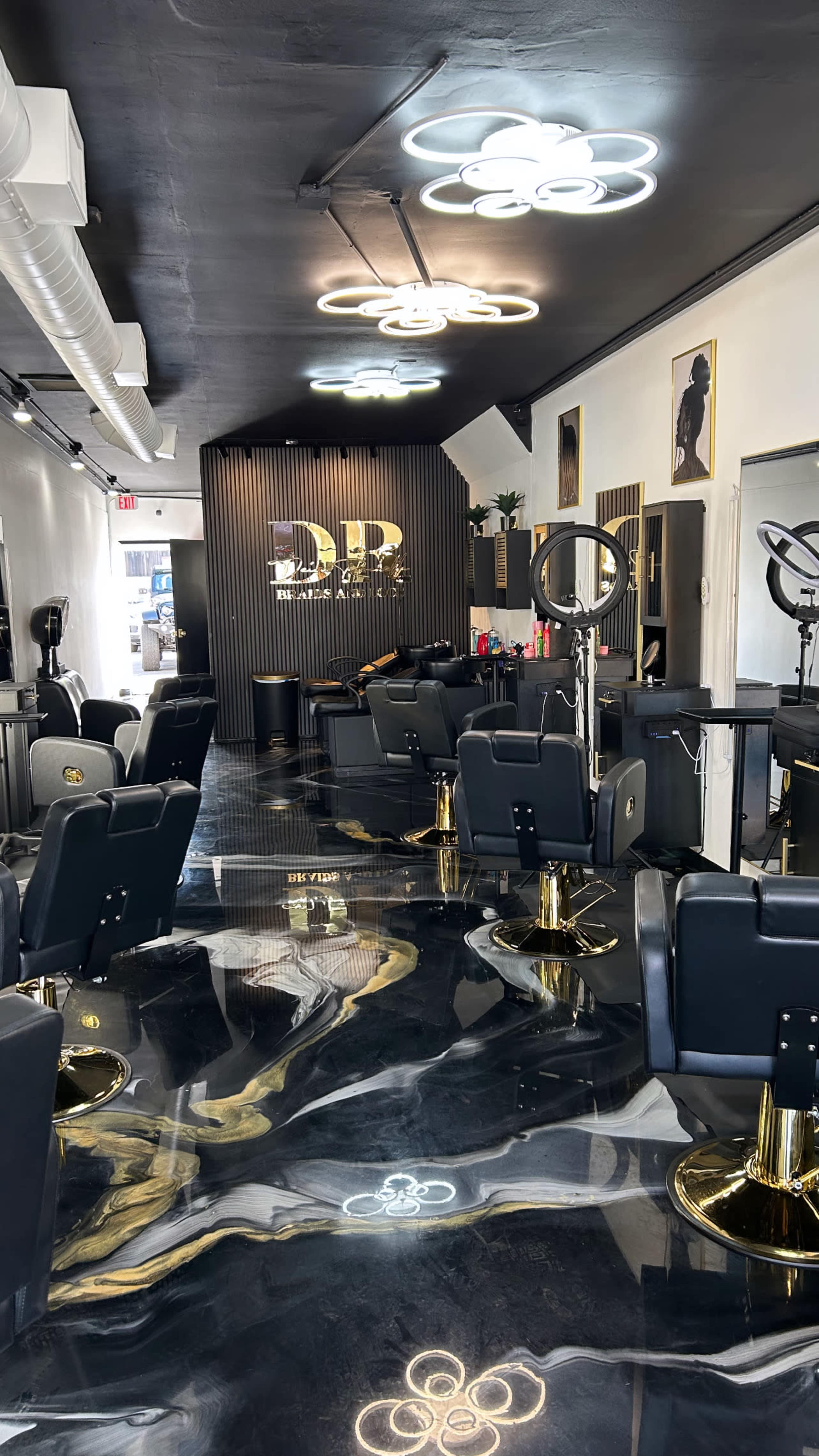 The interior of a modern hair salon features black and gold decor, sleek styling chairs, and illuminated cloud-shaped light fixtures.