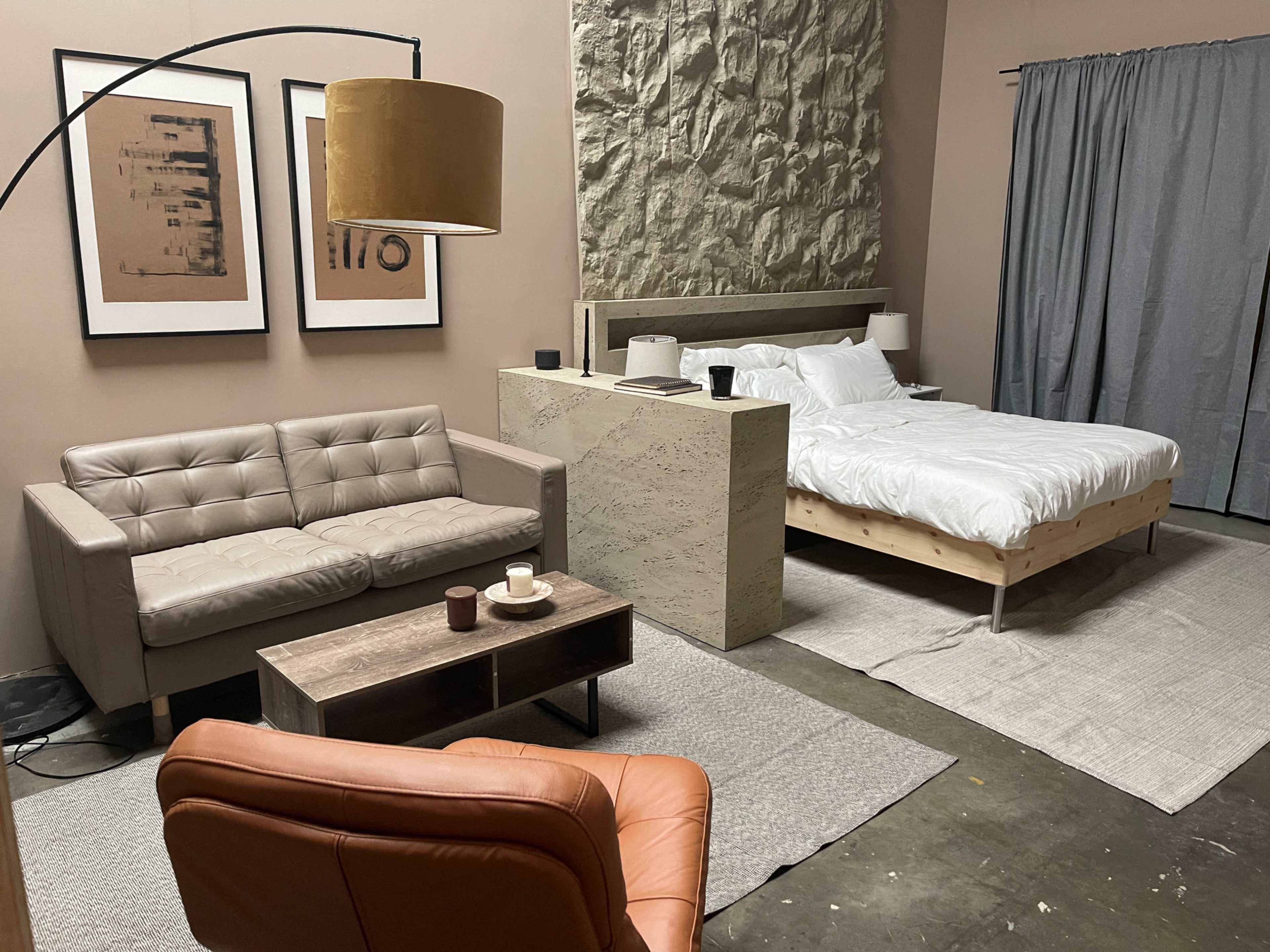 A modern room featuring a bed, a sofa, a coffee table, and a floor lamp against a beige and textured wall.