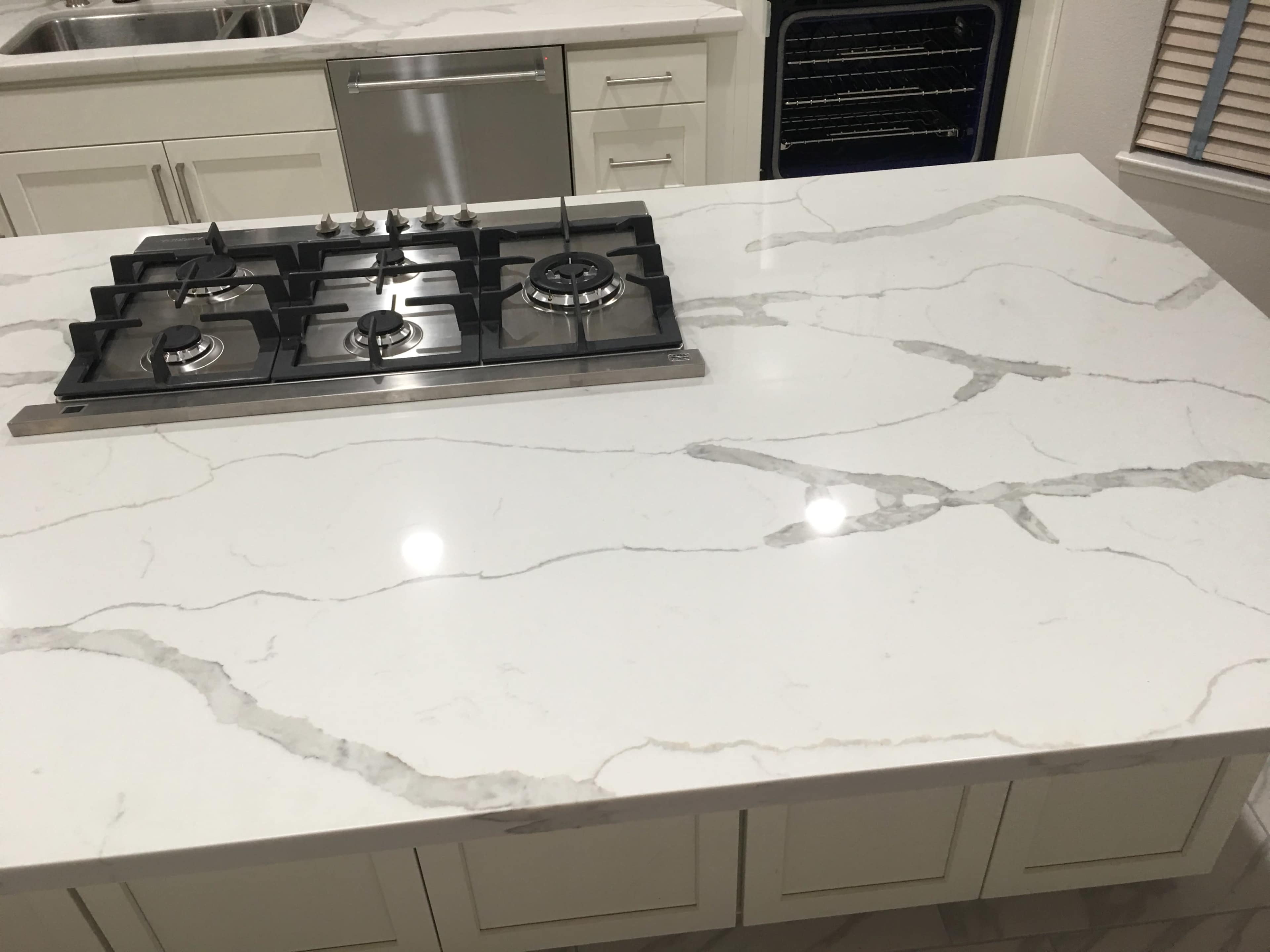 A modern kitchen countertop with a gas cooktop installed, featuring a white marble surface with gray veining.