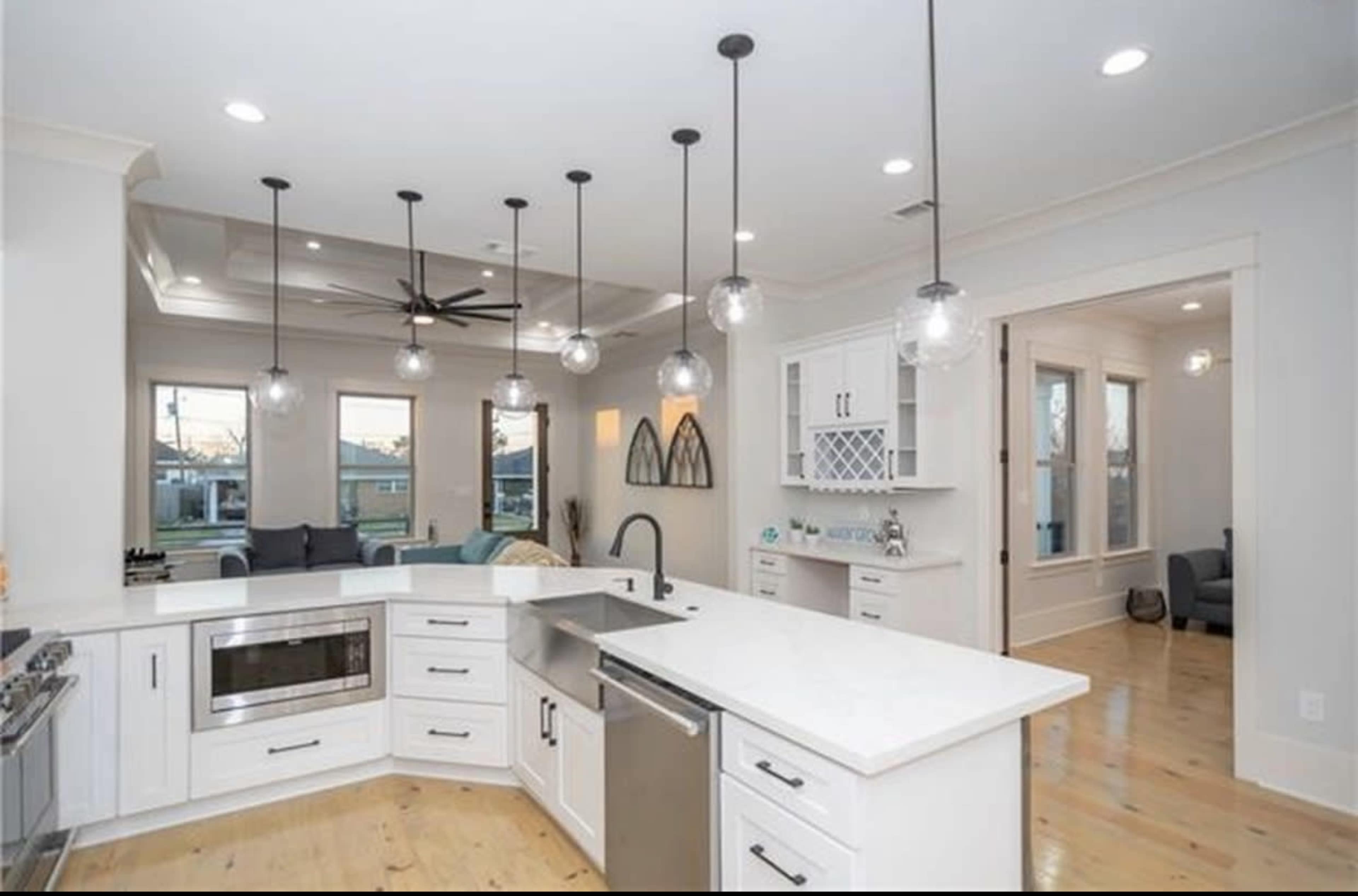 A modern kitchen features white cabinetry, a large island with a sink, and multiple pendant lights hanging from the ceiling.