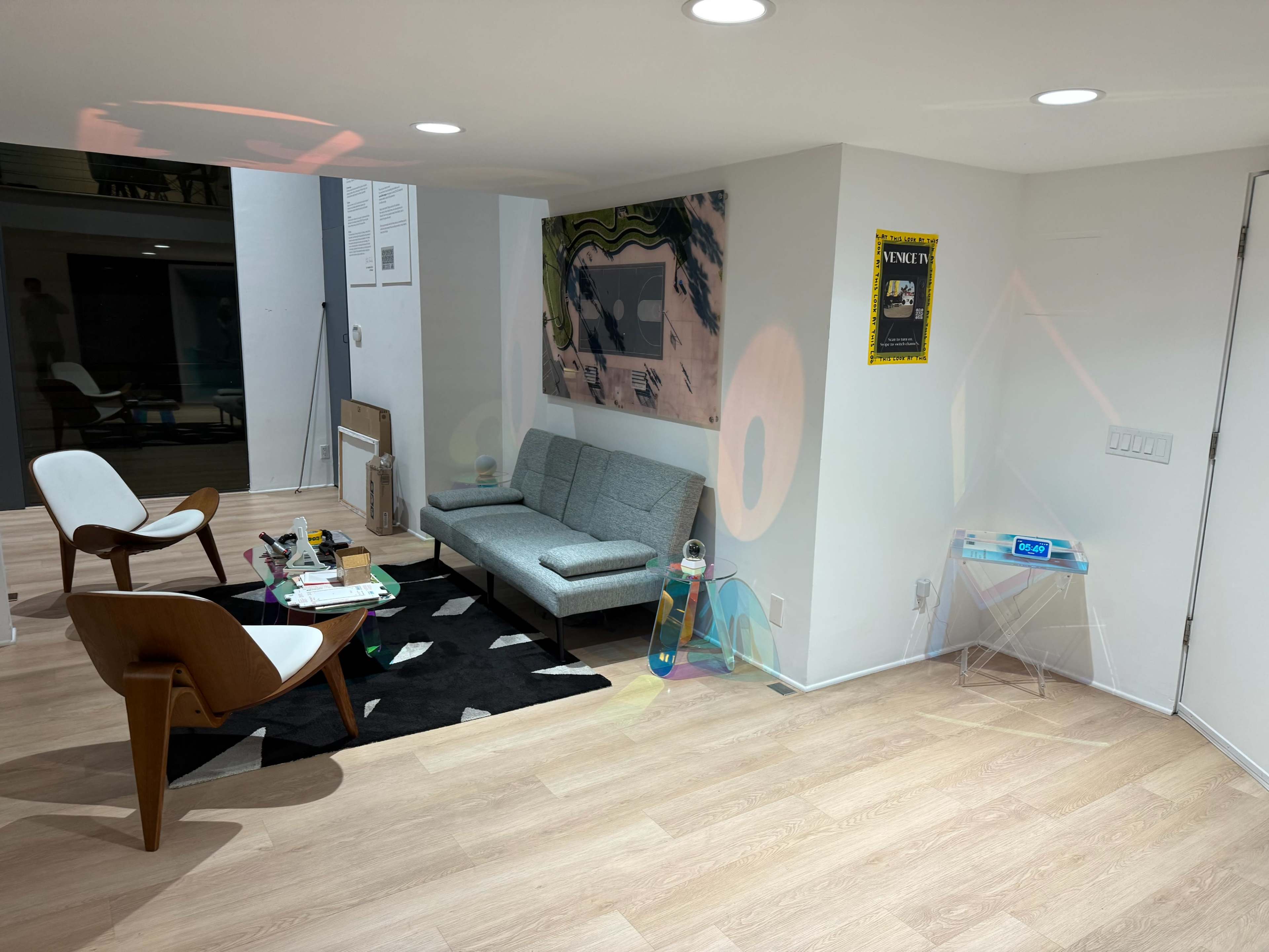 The image depicts a modern living space with a gray sofa, a black and white rug, and wooden flooring, accompanied by chairs and various decor items.