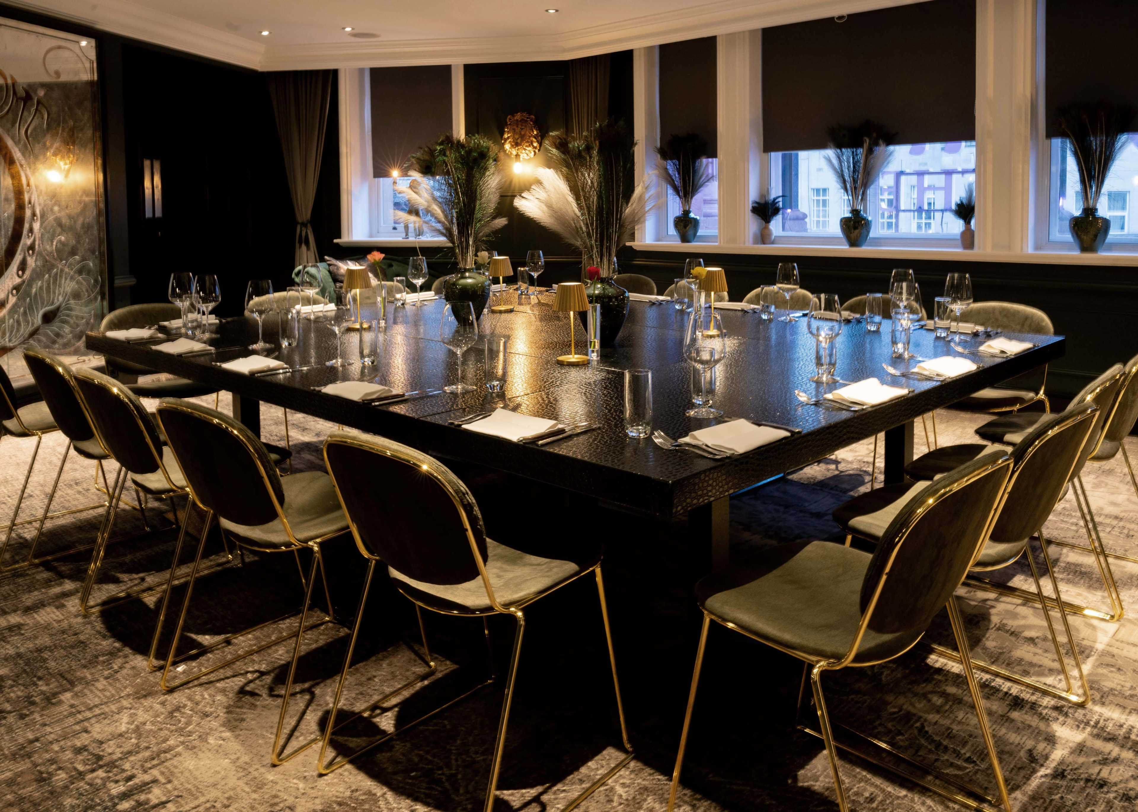 A large dining table is set for a meal, surrounded by elegantly designed chairs in a well-lit restaurant with decorative plants in the background.