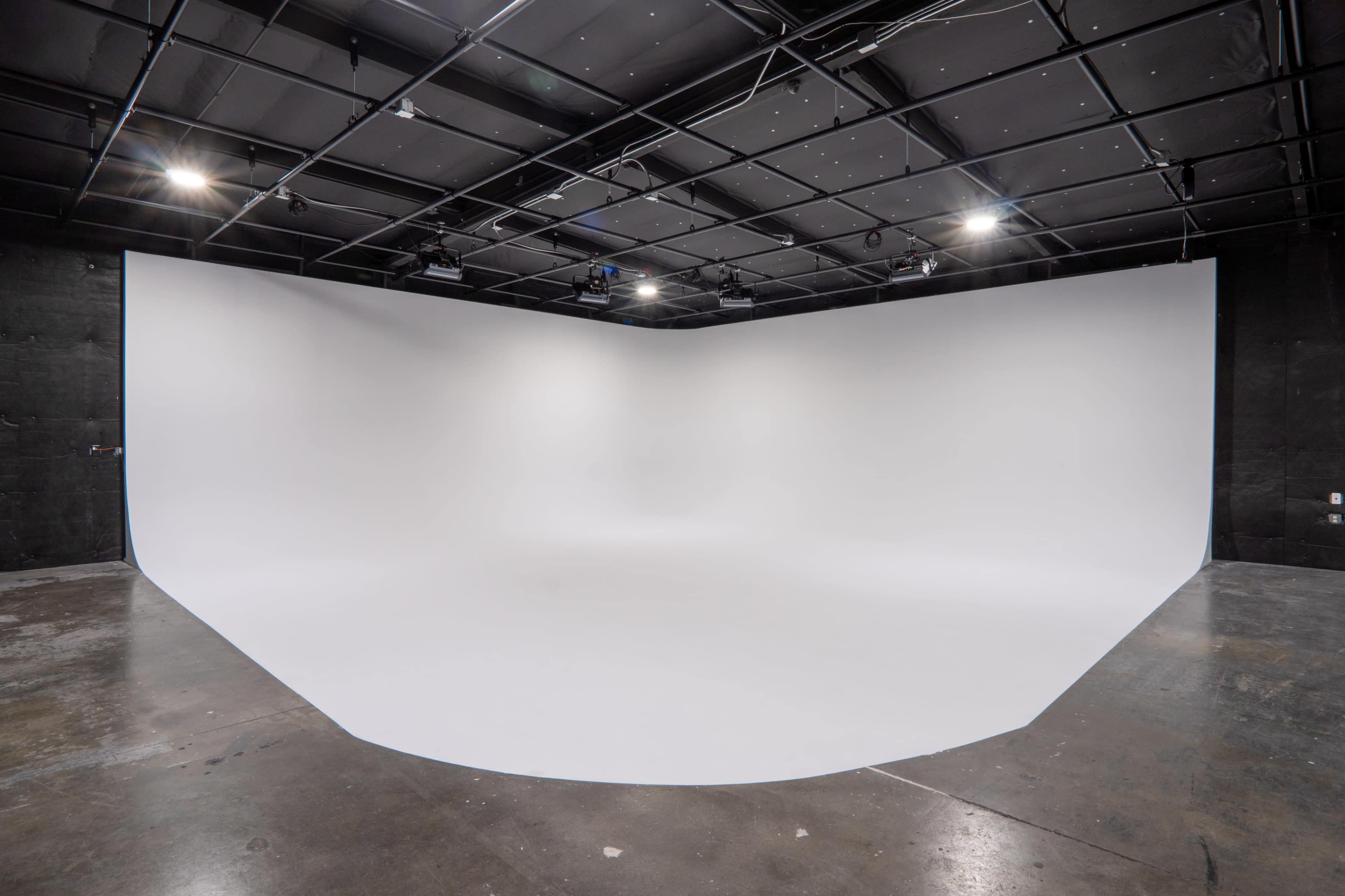A large, empty photography studio with a curved white backdrop and a polished concrete floor.
