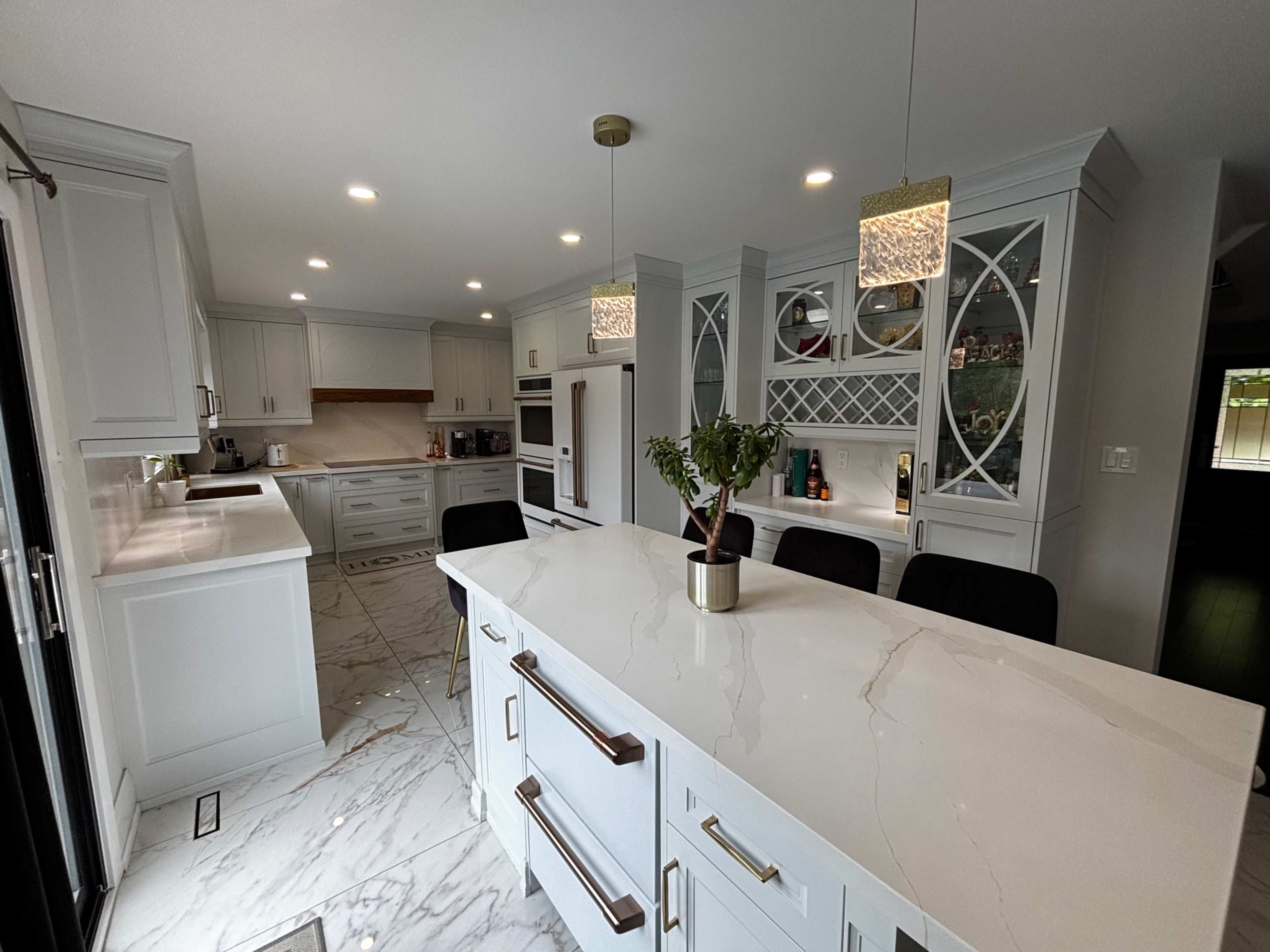 The image shows a modern kitchen featuring white cabinetry, a large marble island, and pendant lighting.