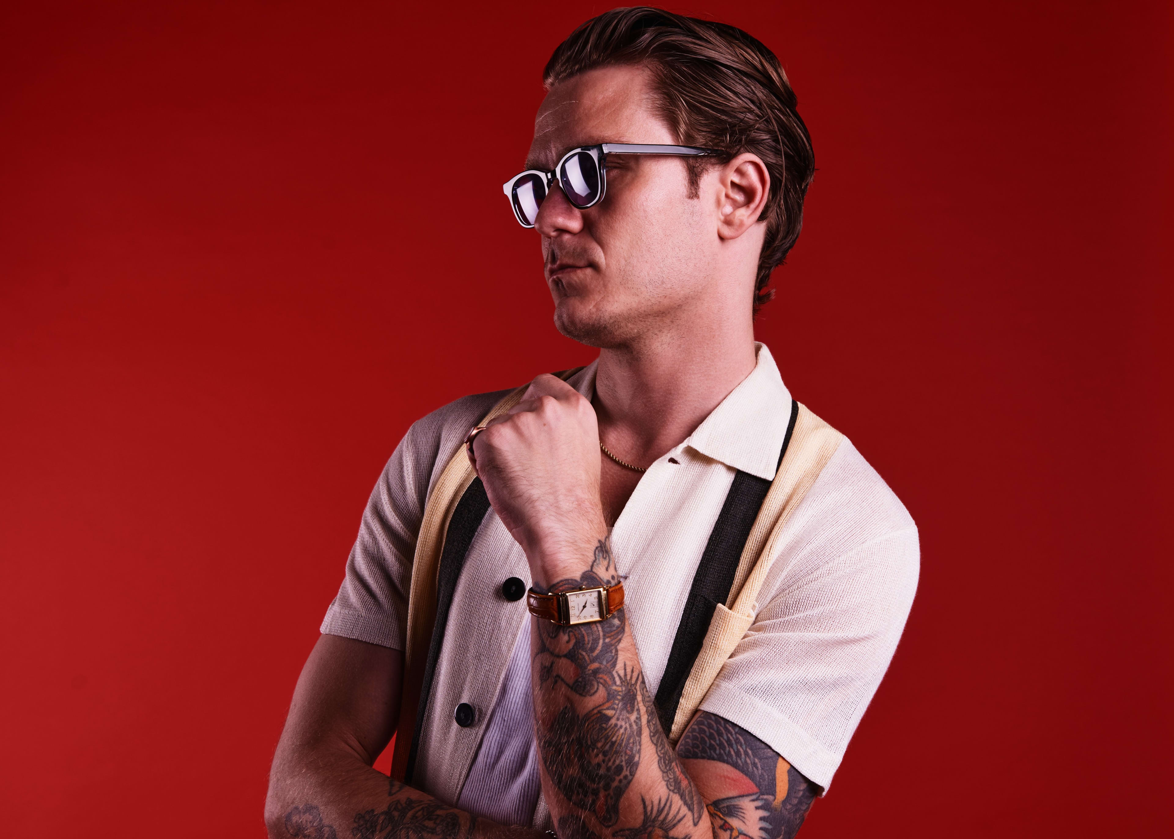A man with a tattoo on his arm posing for a 1950s fashion photoshoot.