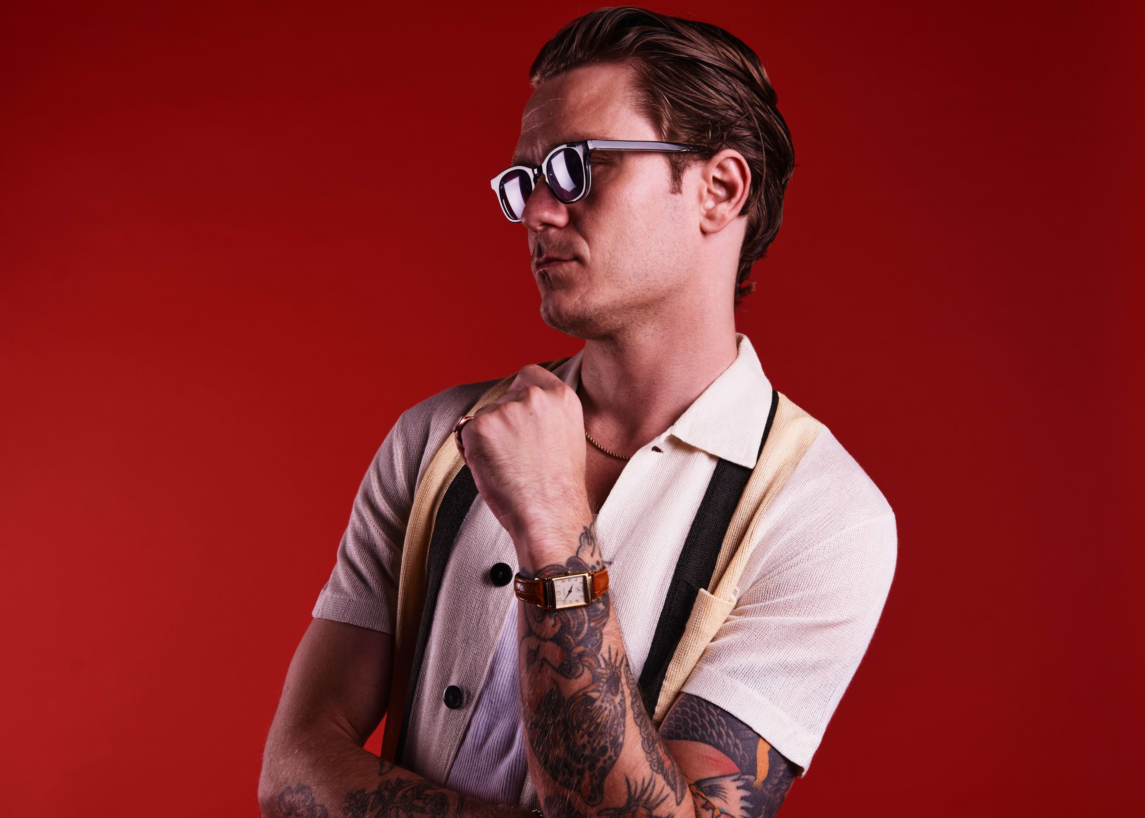 A man with a tattoo on his arm posing for a 1950s fashion photo shoot.